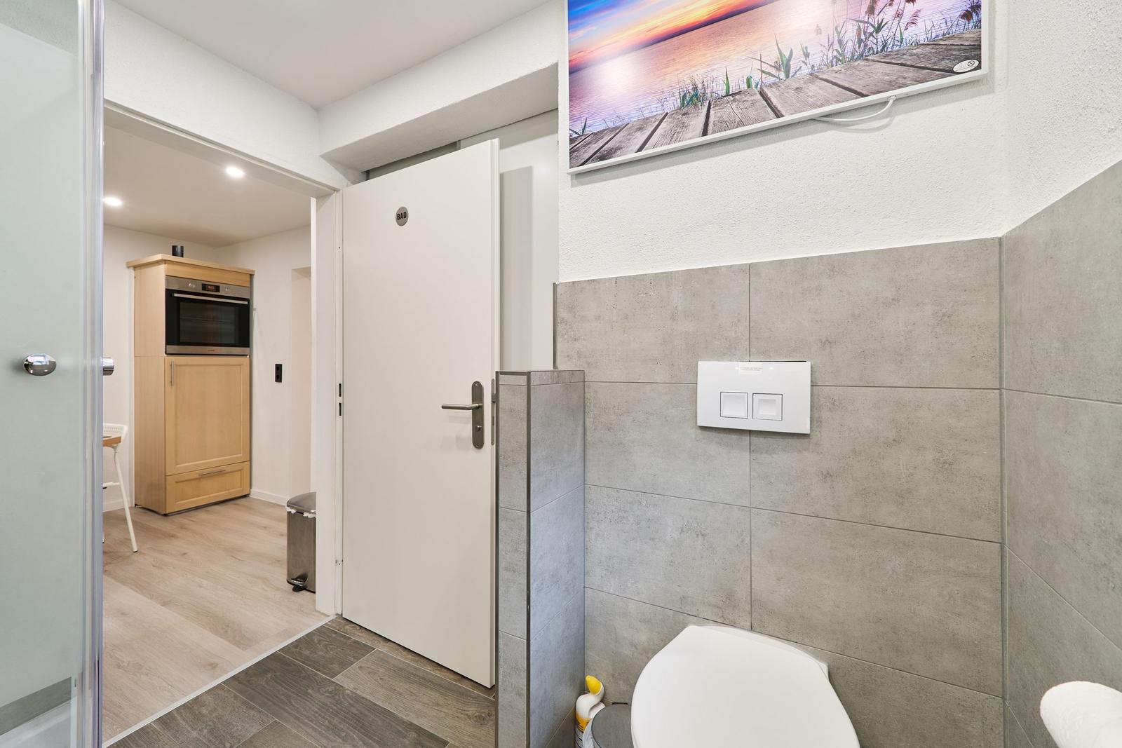Bad mit Toilette und Wandbild. Tür führt in Wohnbereich mit Küchenzeile.
