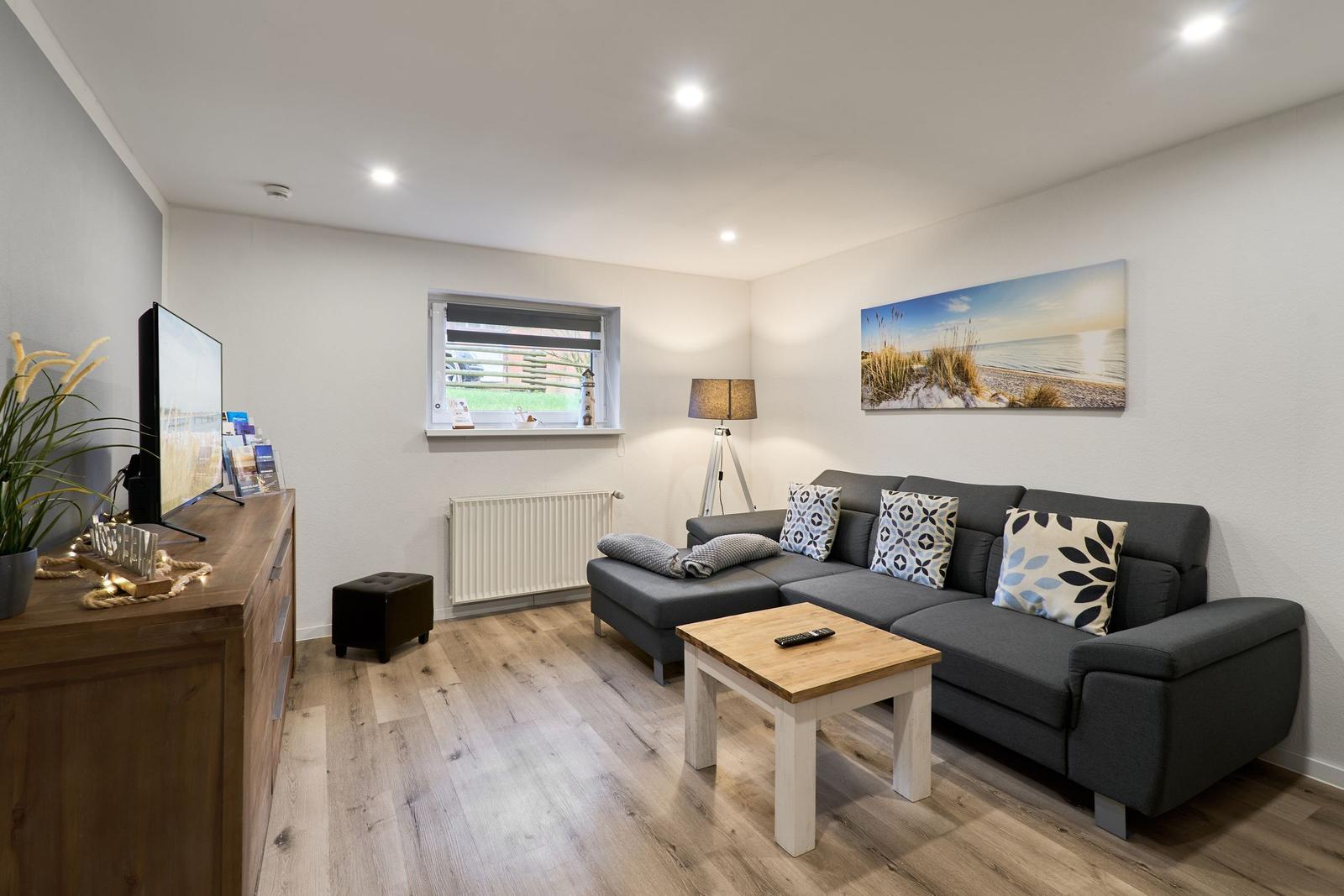 Wohnzimmer mit Sofa, Couchtisch und Fernseher. Holzboden und Wandbild.