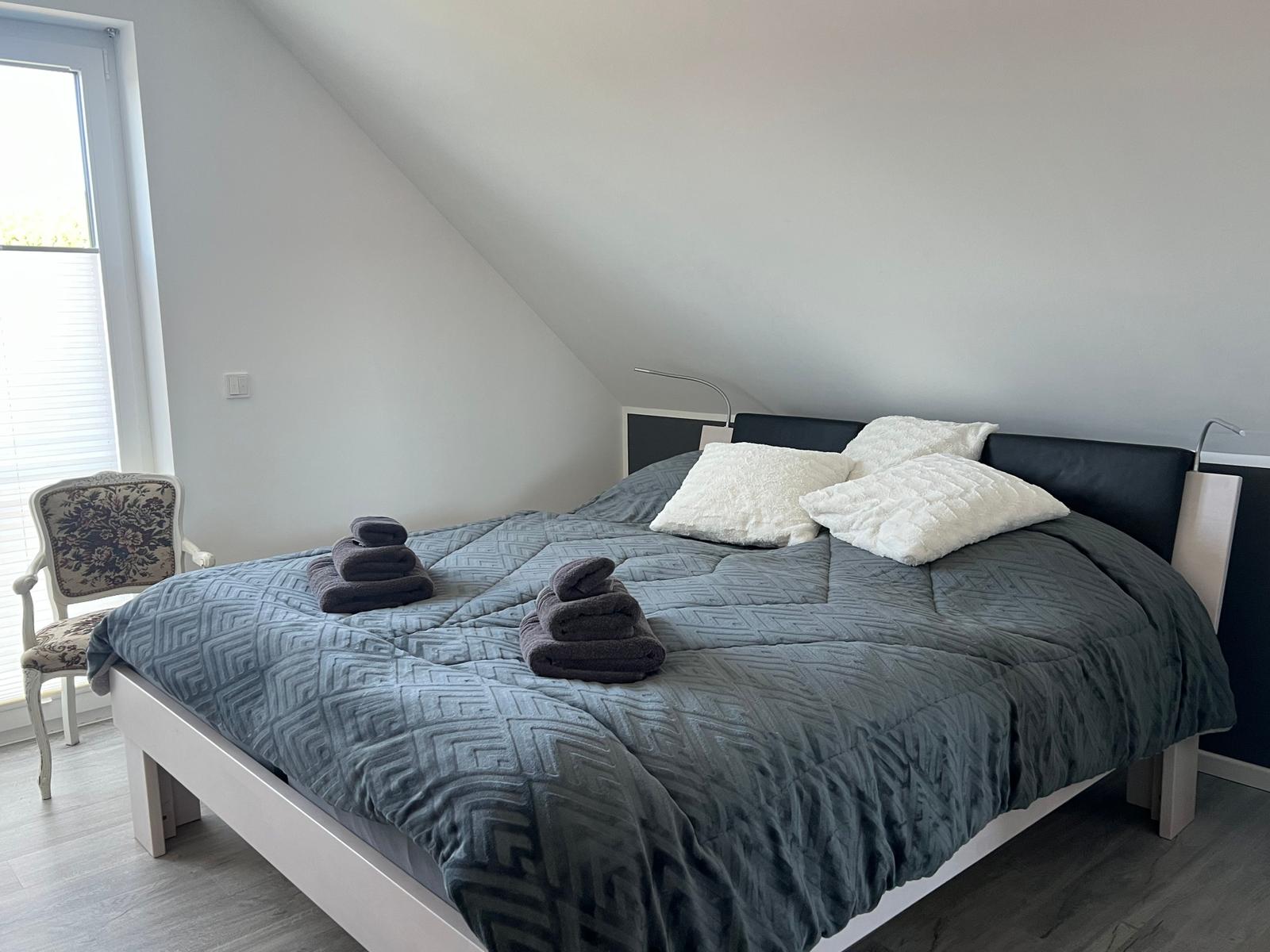 Schlafzimmer mit Dachschrägen, Bett mit grauer Bettwäsche und zwei Handtüchern.