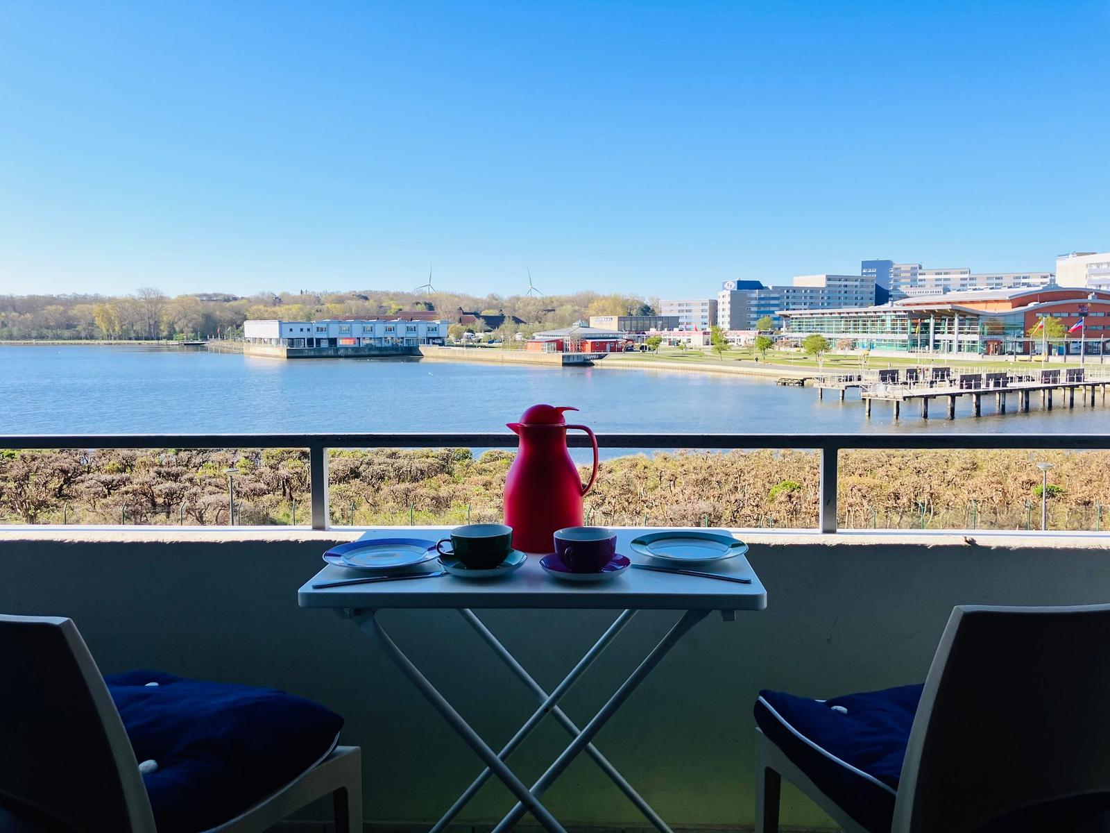 Balkon mit Tisch und Stühlen, Blick auf Wasser und Stadt.