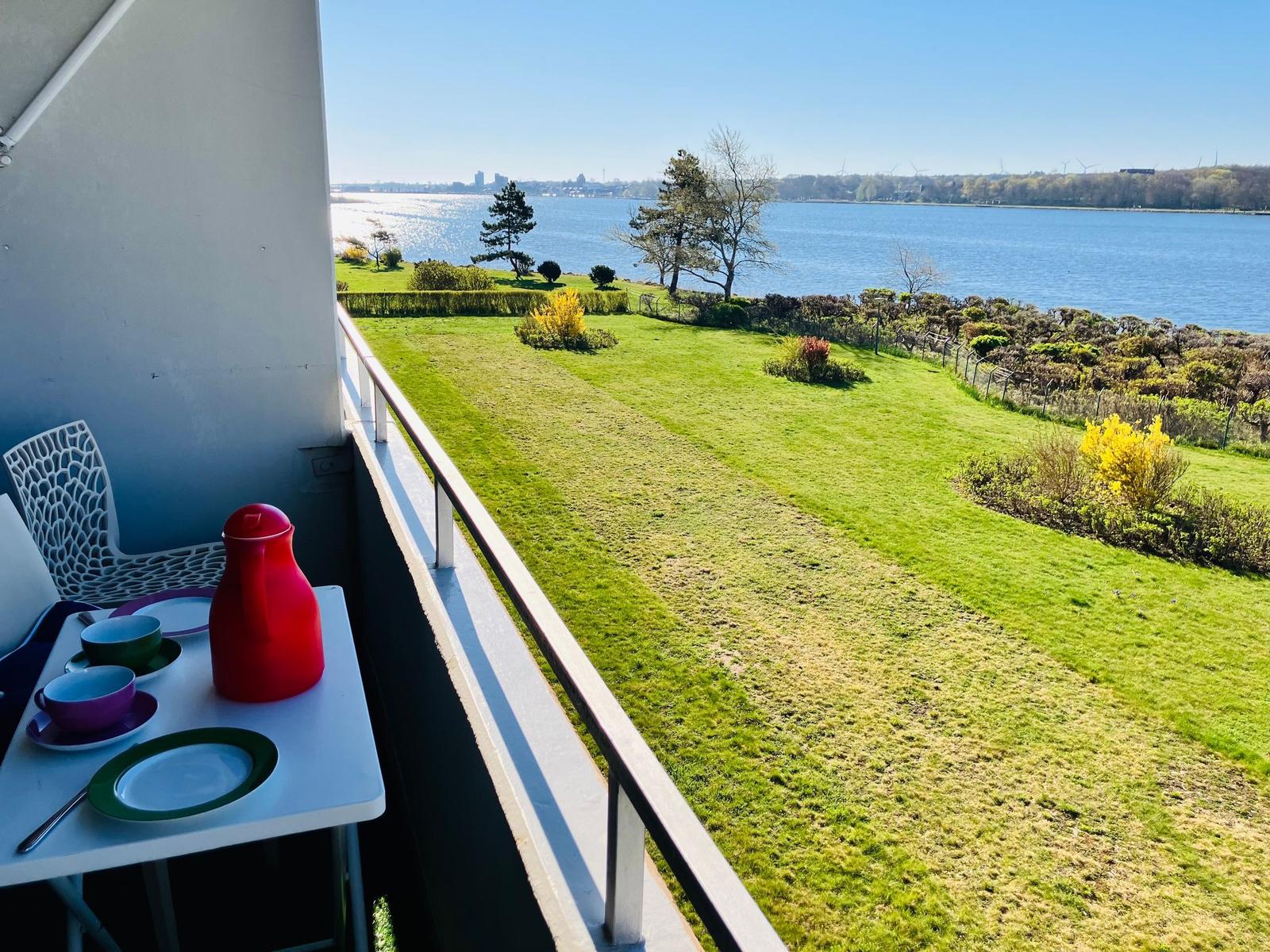 Balkon mit Tisch und Stühlen bietet Blick auf Grünfläche und Wasser.
