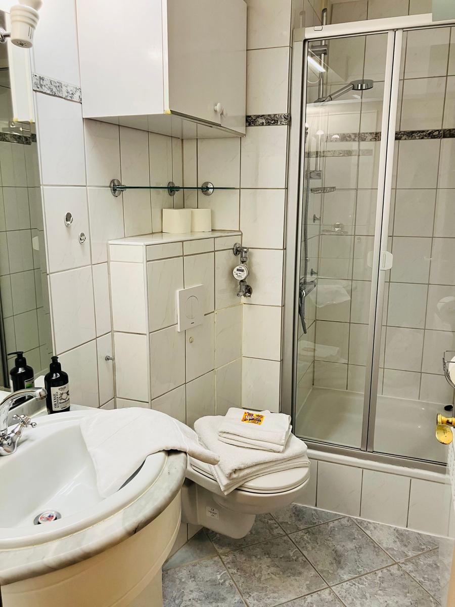 Badezimmer mit Dusche, Waschbecken und Toilette. Weiße Fliesen und Handtücher.
