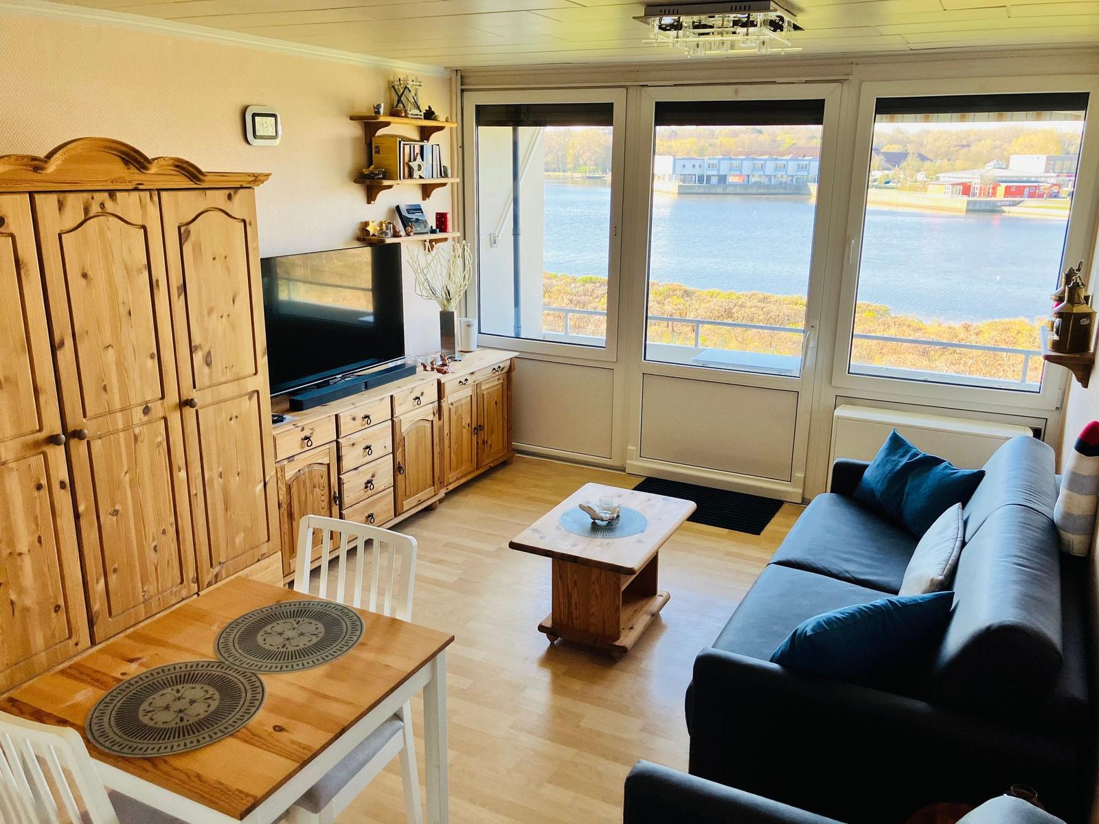 Wohn- und Essbereich mit Blick auf Wasser. Holzmöbel, Sofa und TV.