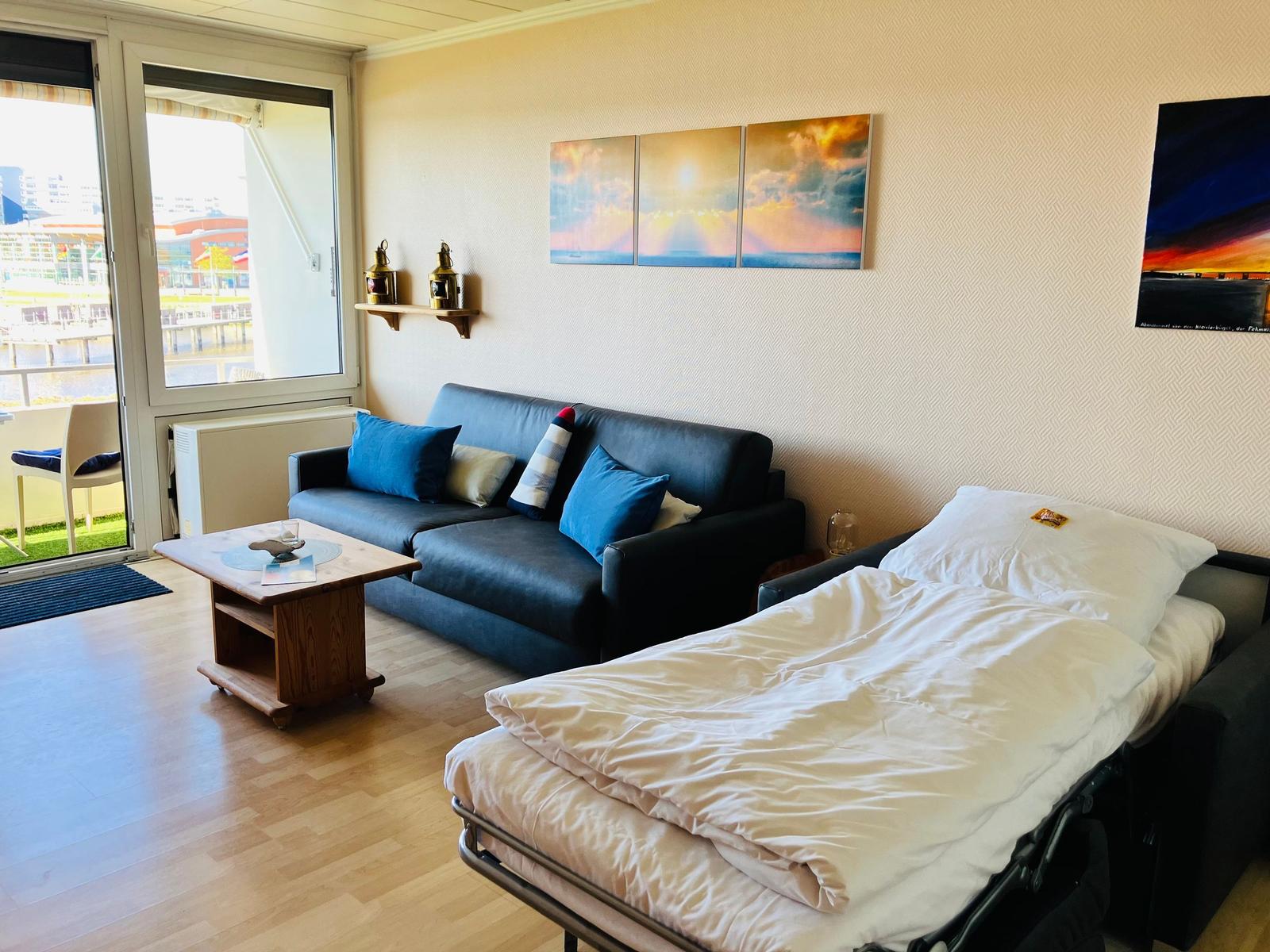Wohnraum mit Sofa, Bett und Balkonblick. Wandbilder und Holztisch.