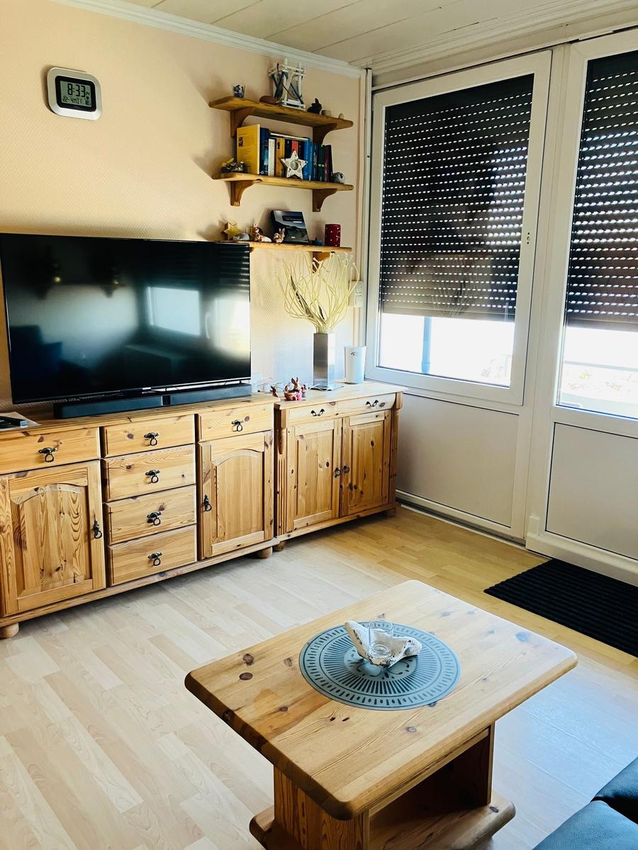Wohnzimmer mit Holzmöbeln, TV und Fenster mit Jalousien.