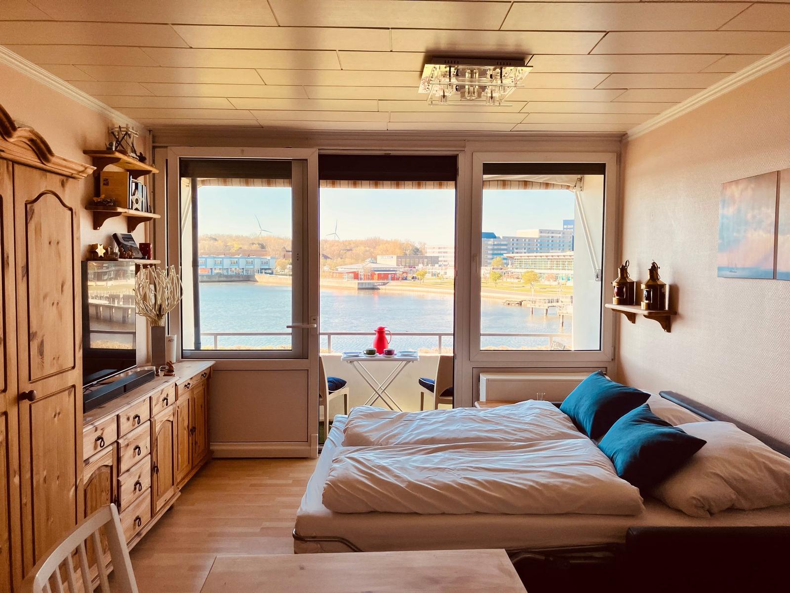 Schlafzimmer mit Blick auf Wasser und Stadt. Holzmöbel, Bett mit Kissen.