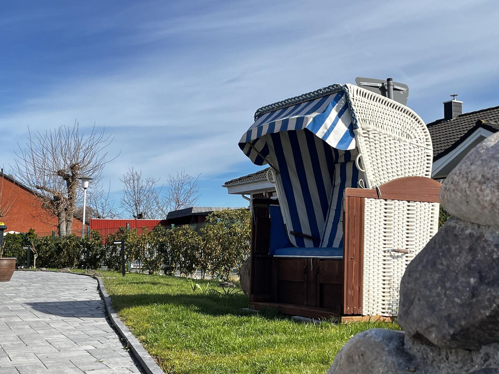 Ein weißer Strandkorb mit blau-weißem Schirm steht auf einer grünen Wiese.
