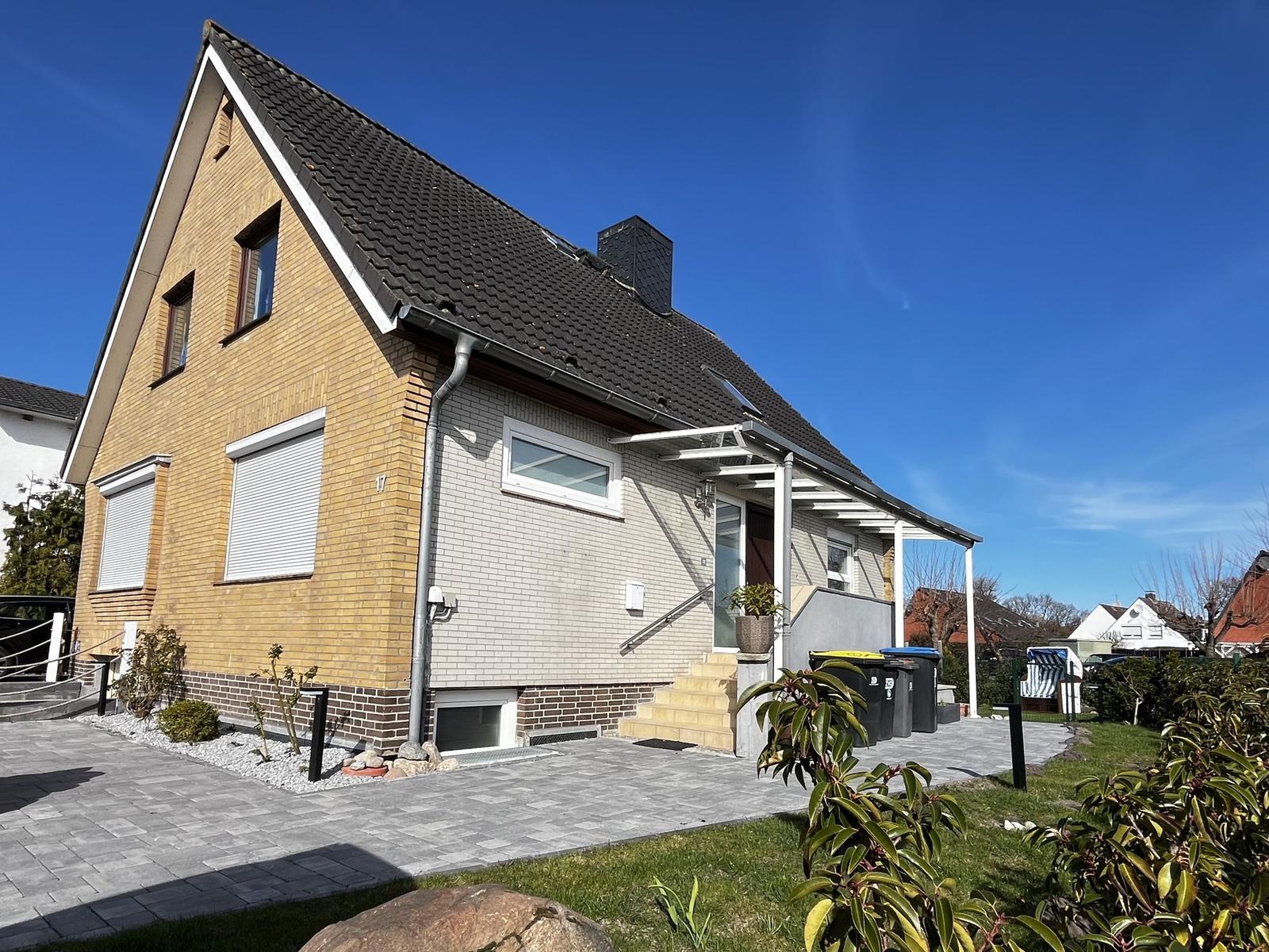 Ein zweistöckiges Haus mit gelbem und grauem Backsteinfassade, Dachterrasse und Garten.
