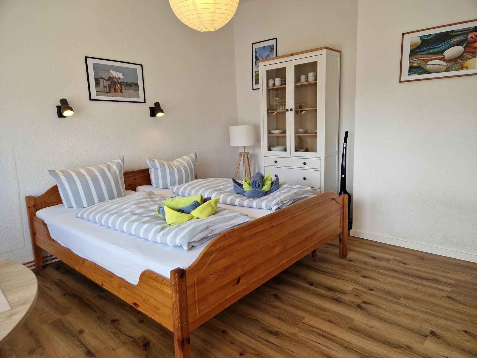 Schlafzimmer mit Holzbett, Schrank und Wandbildern.