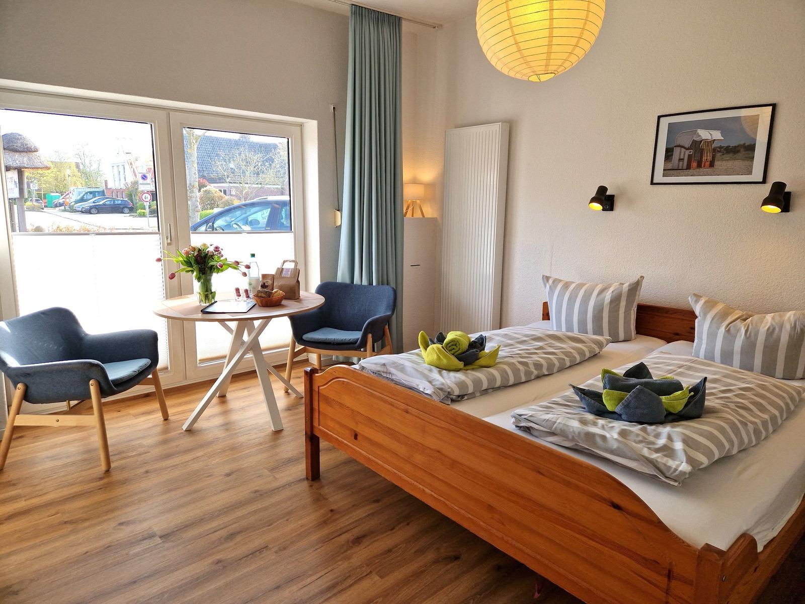 Ein Schlafzimmer mit Doppelbett, zwei Stühlen und Tisch. Durchgangstür mit Blick nach draußen.