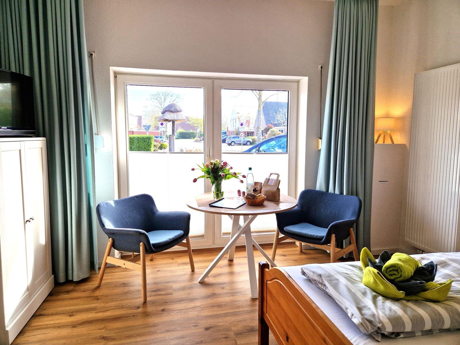 Zimmer mit Bett, Tisch, zwei Stühlen und Fensterblick auf Straße.