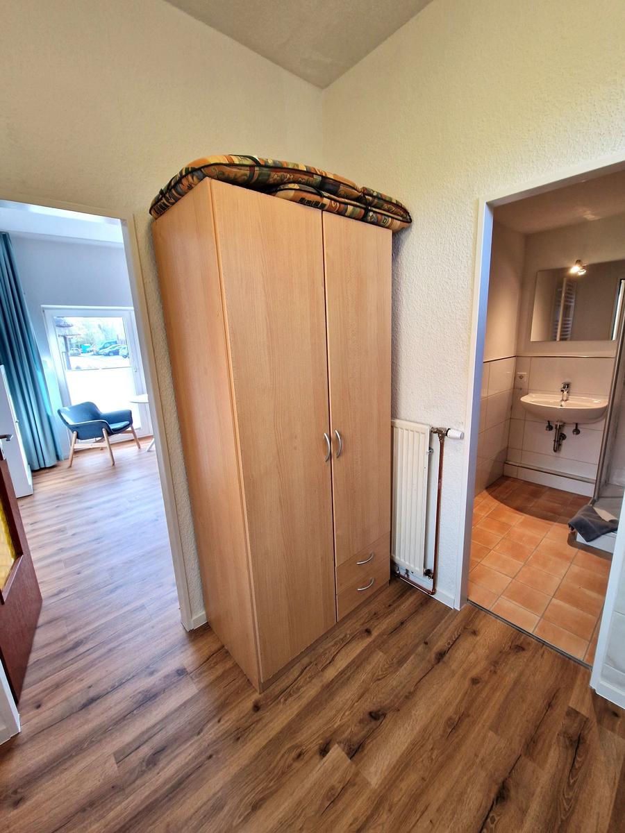 Schlafzimmer mit Kleiderschrank, Bad und Wohnbereich mit Holzboden und blauer Sitzgelegenheit.