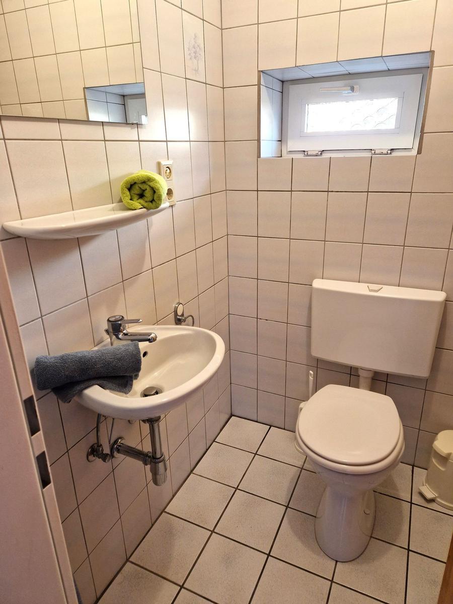 Bathroom with toilet, sink, and window. Green and gray towels.
