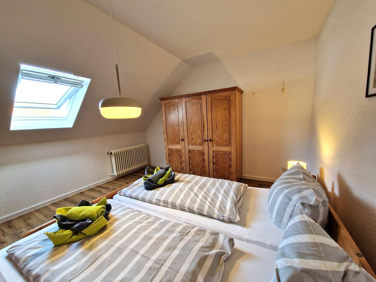 Bedroom with sloped ceiling, double bed, wooden wardrobe, and skylight.