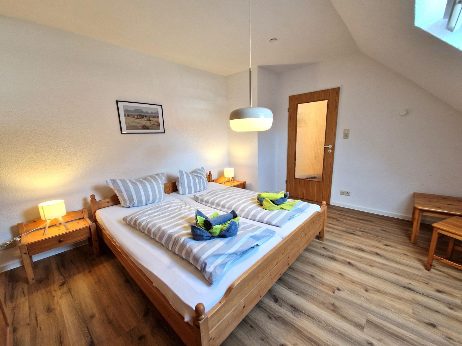 Bedroom with double bed, wooden floor, and skylight. Two nightstands and pendant lamp.