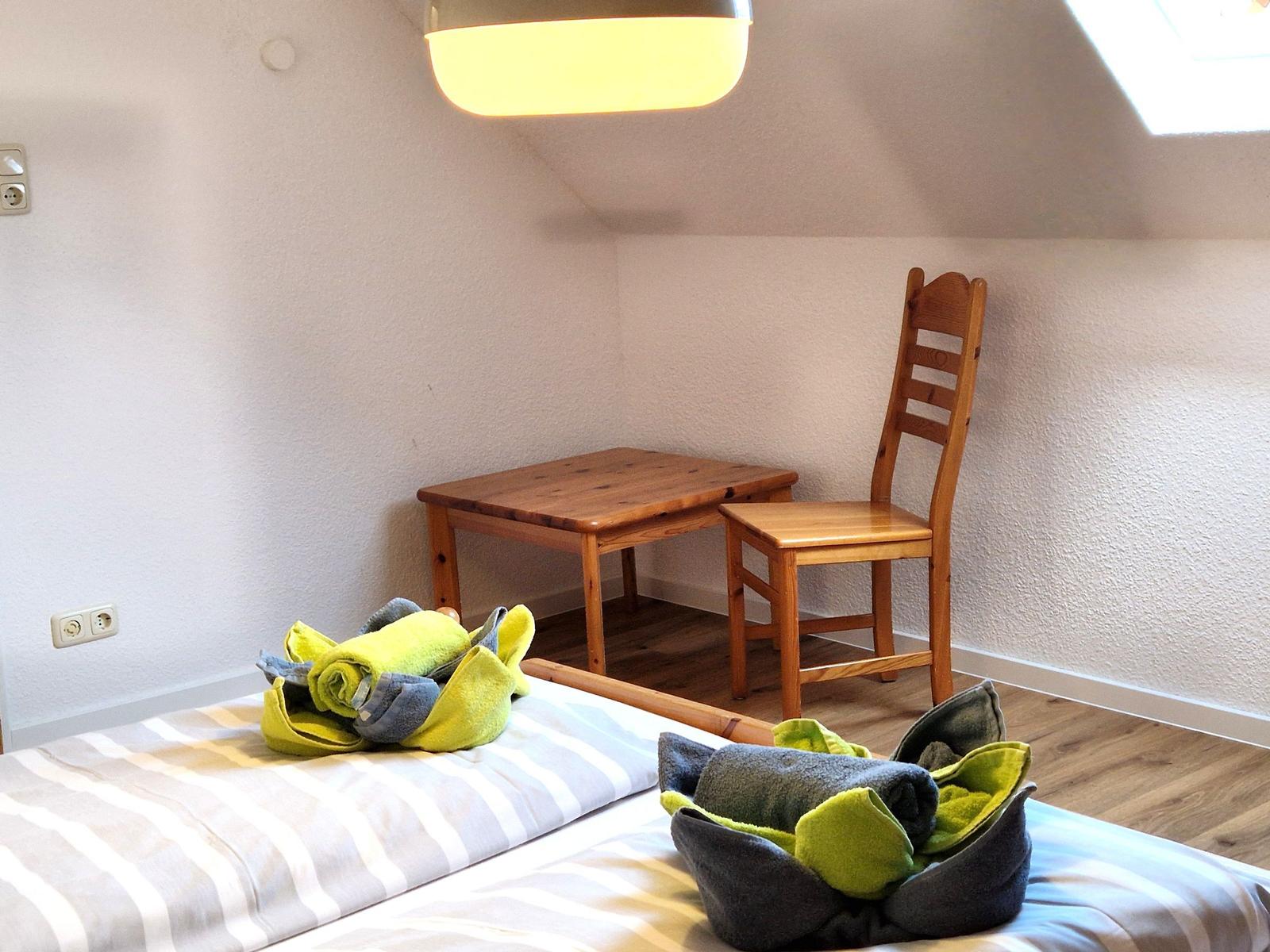 Bedroom with bed, wooden table and chair under sloped ceiling.