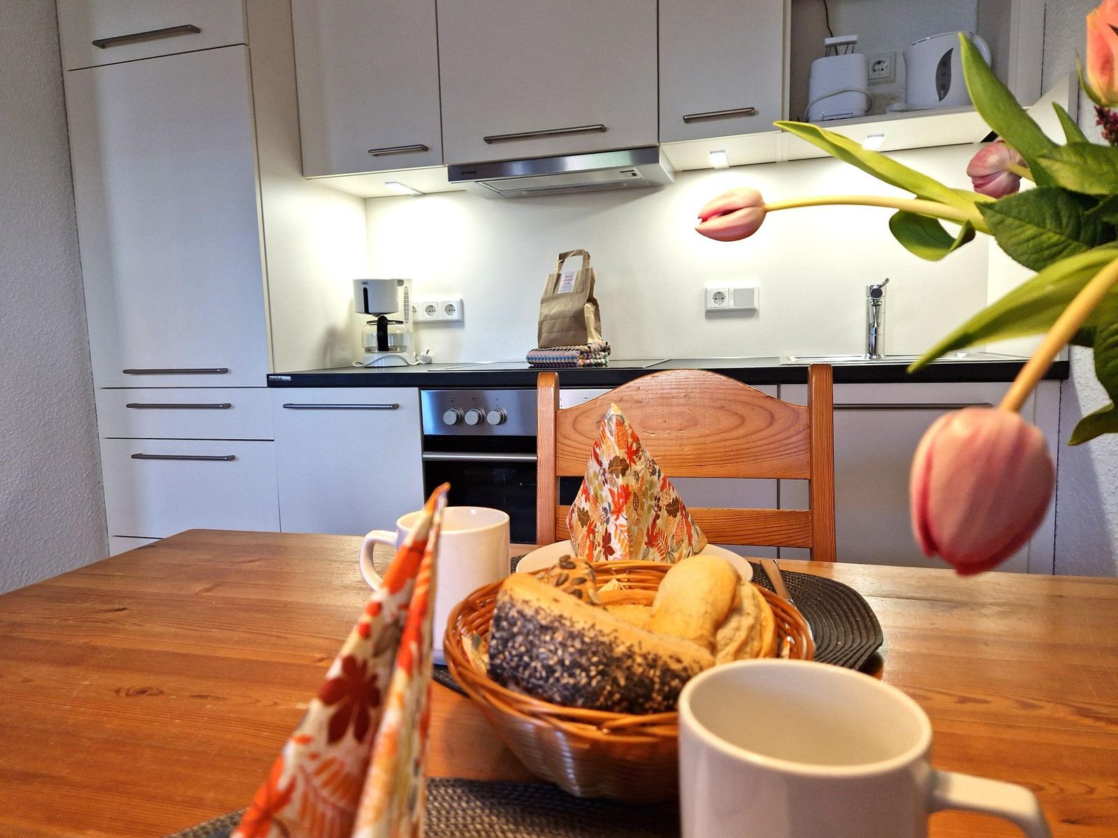 Kitchen with dining area, wooden table, coffee machine, and flowers.