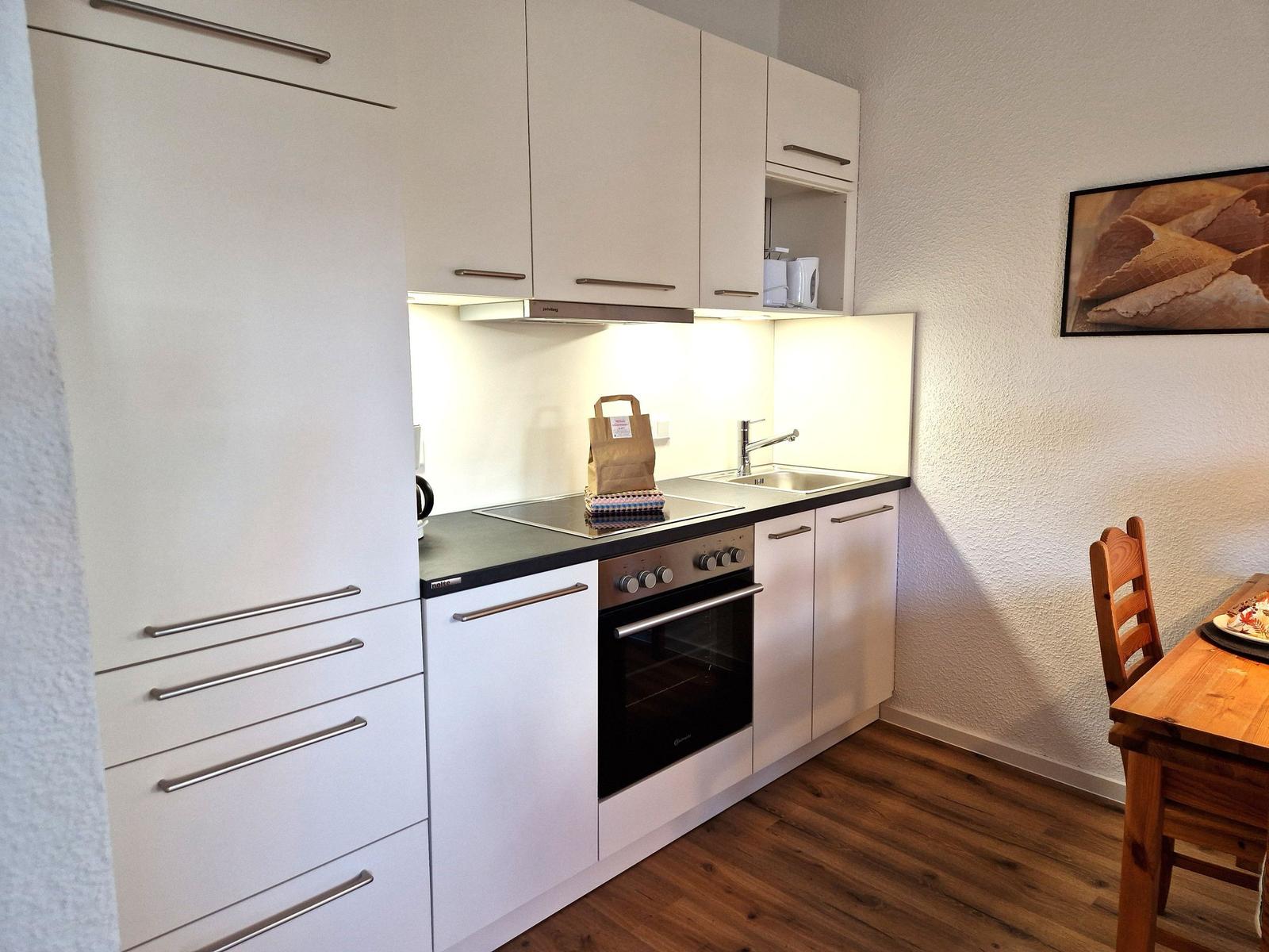 Kitchen with white cabinets, stove, and sink. Wooden floor and dining area with table.