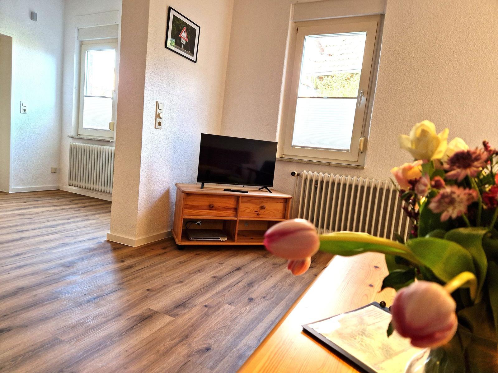 Living room with wooden floor, TV on wooden stand, and flowers on table.