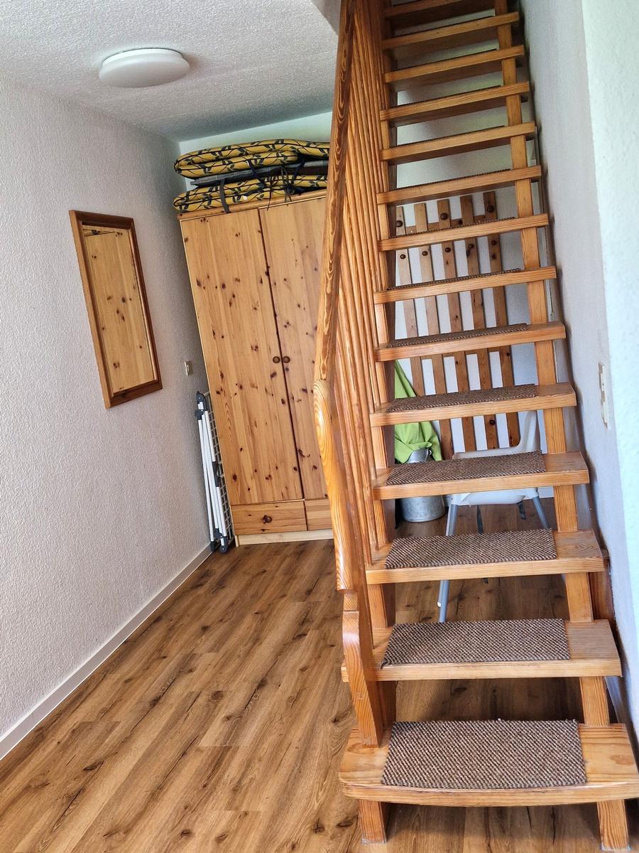Holztreppe mit Teppichstufen führt zur oberen Etage. Holzschrank und Wandbild sind sichtbar.