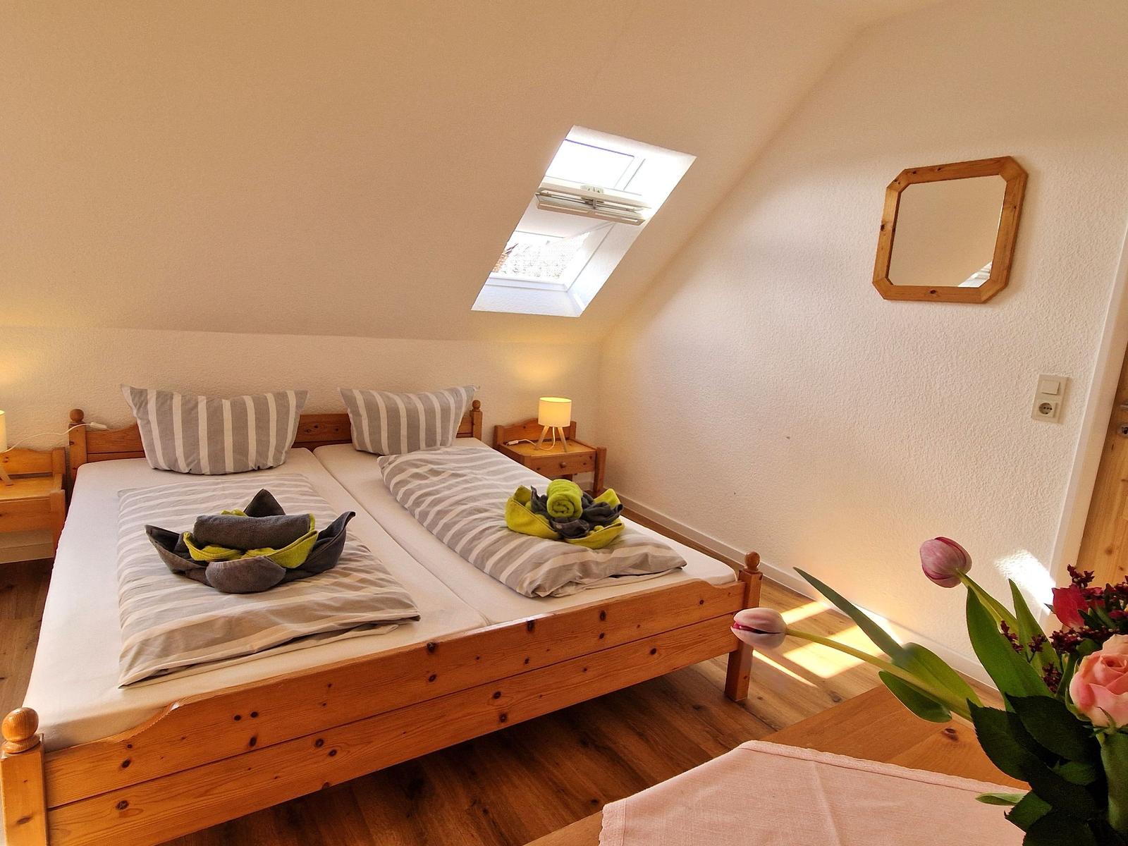 Schlafzimmer mit Doppelbett, Holzbett, Dachfenster und Spiegel an der Wand.