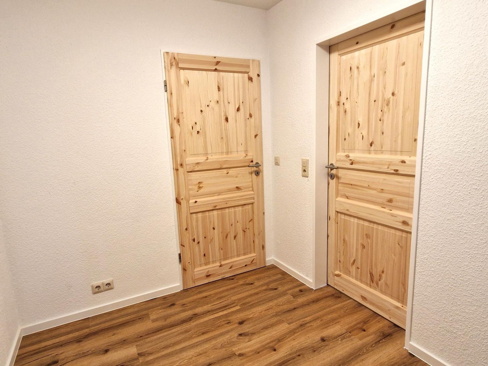 Zwei Holztüren in einem Raum mit Holzboden und weißen Wänden.