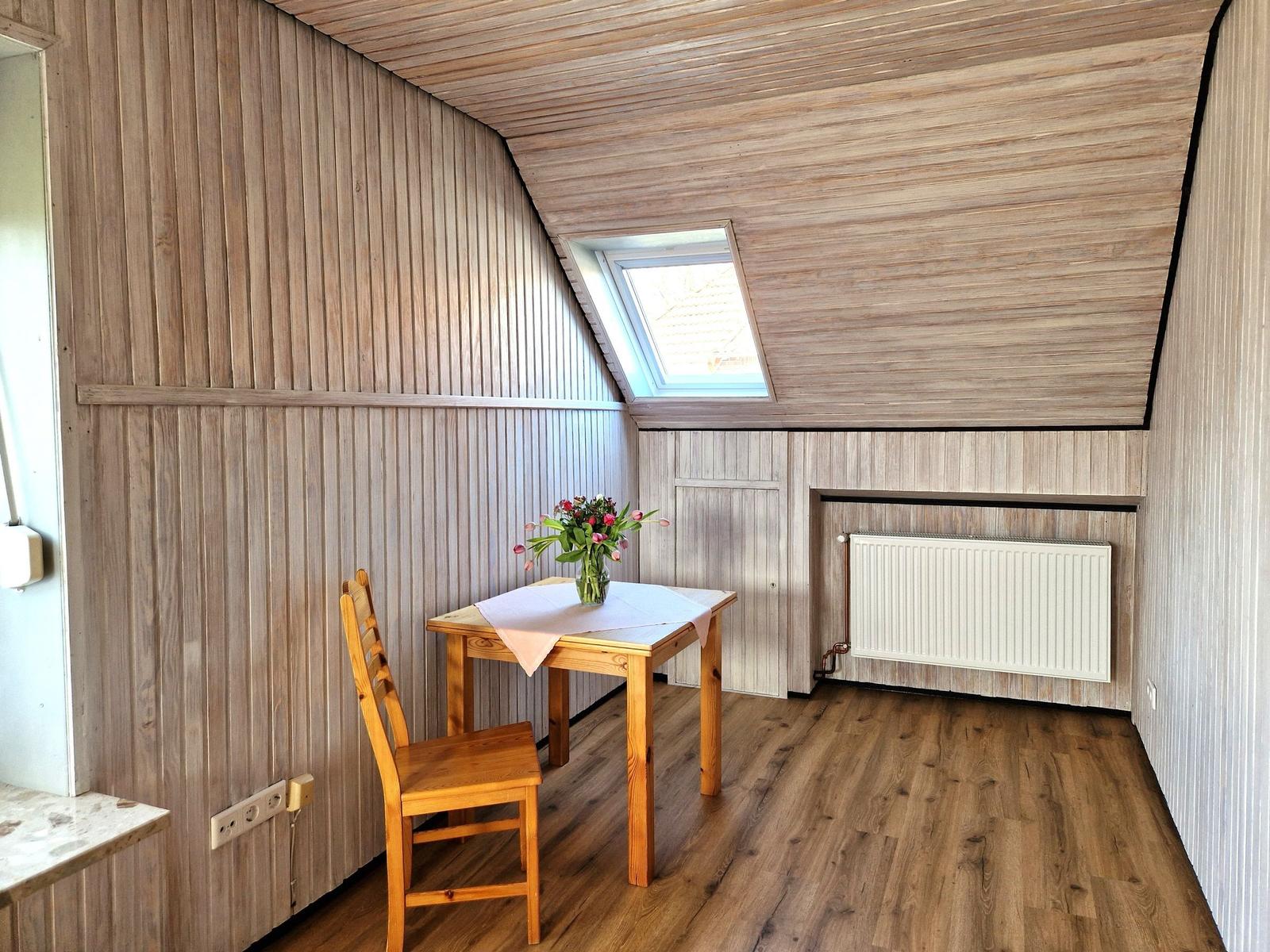 Raum mit Holzwand, Tisch, Stuhl und Dachfenster.