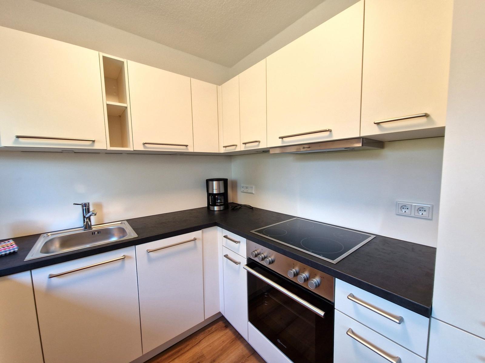 Küche mit weißen Schränken, schwarzer Arbeitsplatte, Spüle und Induktionskochfeld.