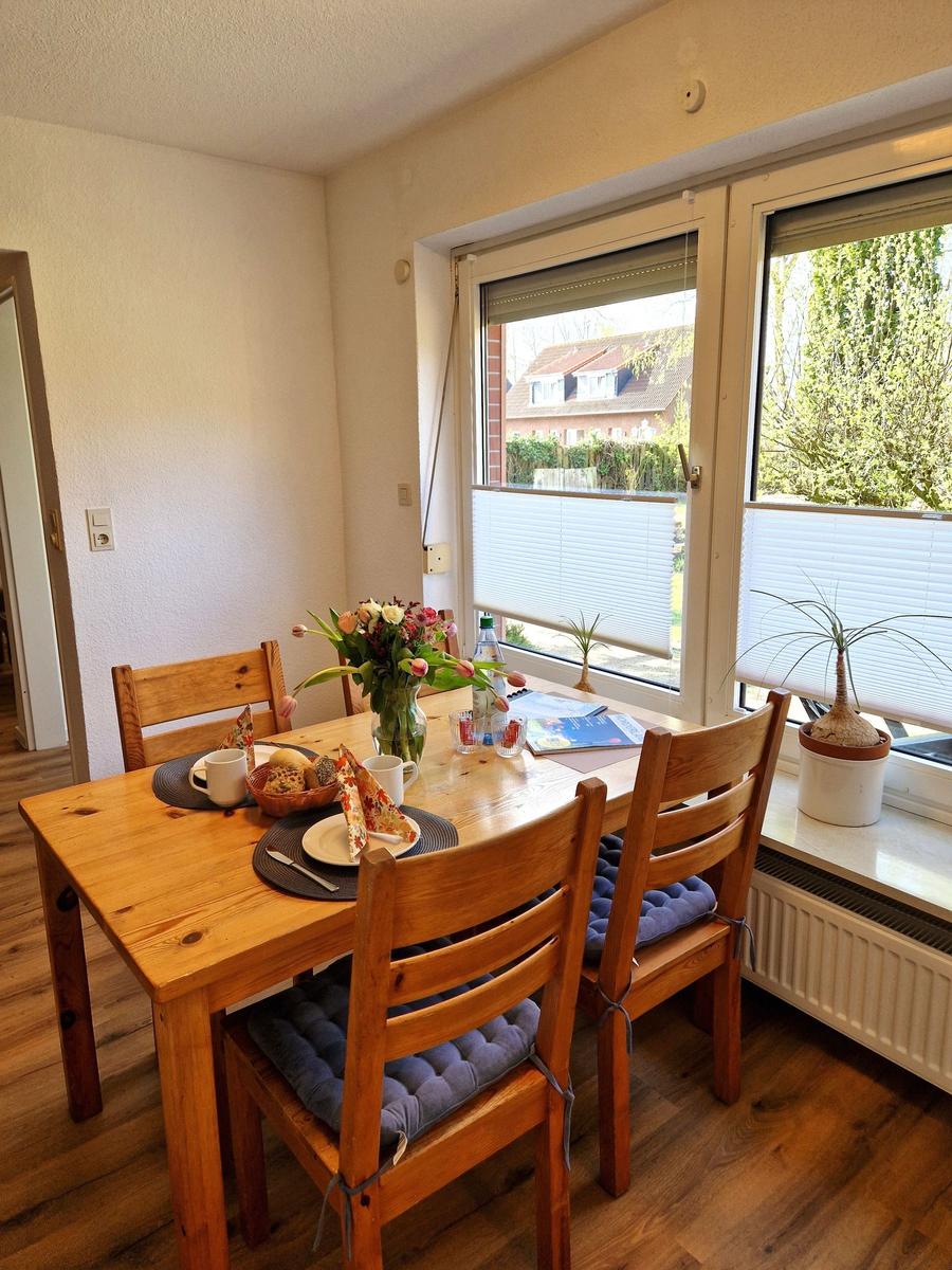 Esstisch mit vier Holzstühlen, Blumen und Blick auf Balkon.