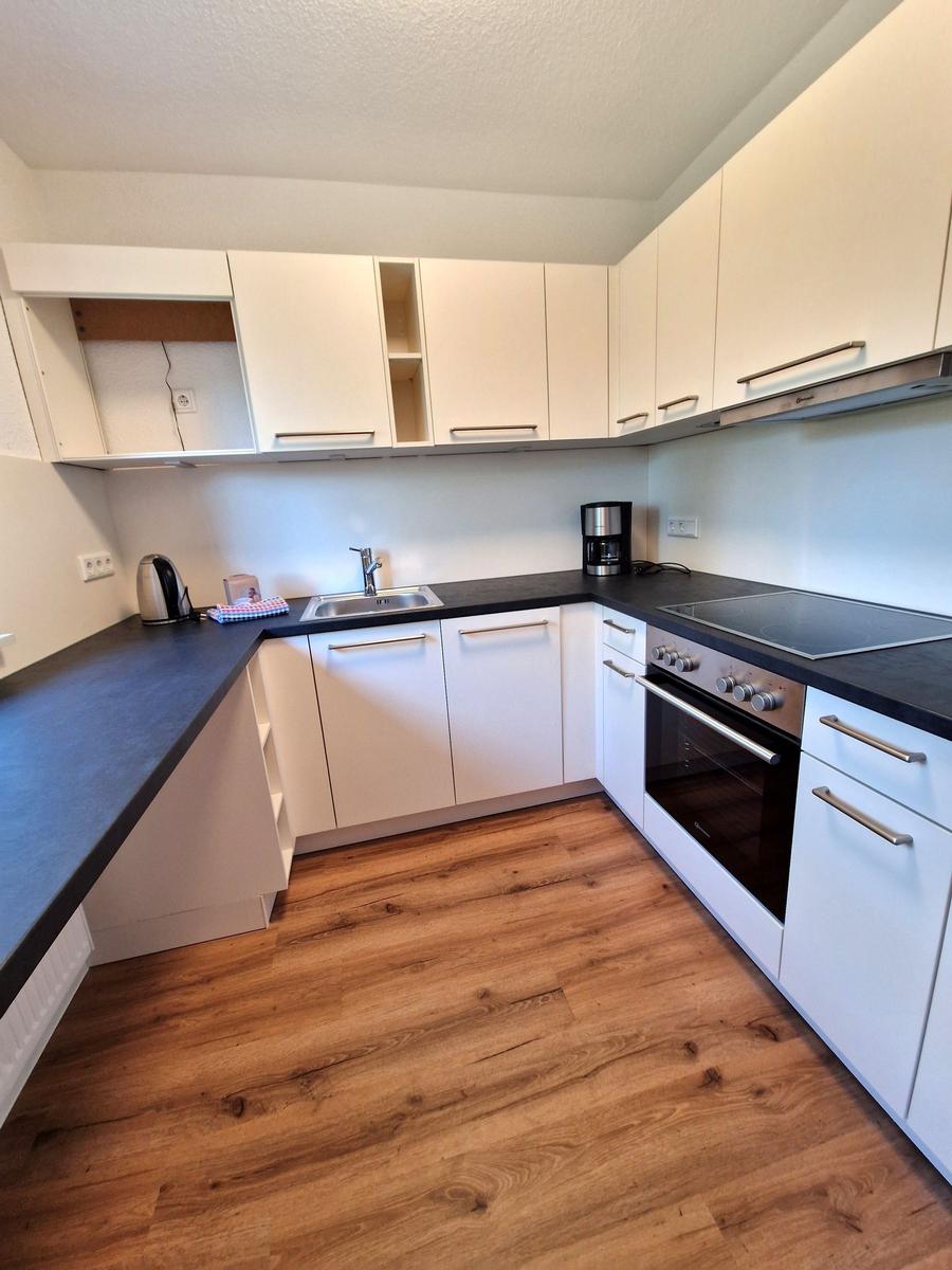 Küche mit weißen Schränken, dunklem Arbeitsplatz und Holzboden