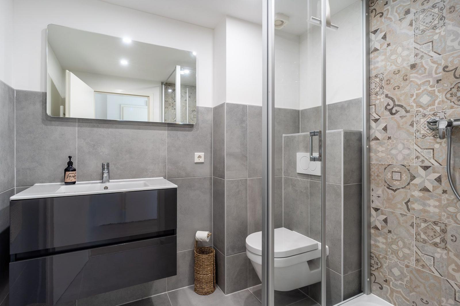Badezimmer mit Dusche, Toilette und Waschbecken mit Spiegel.