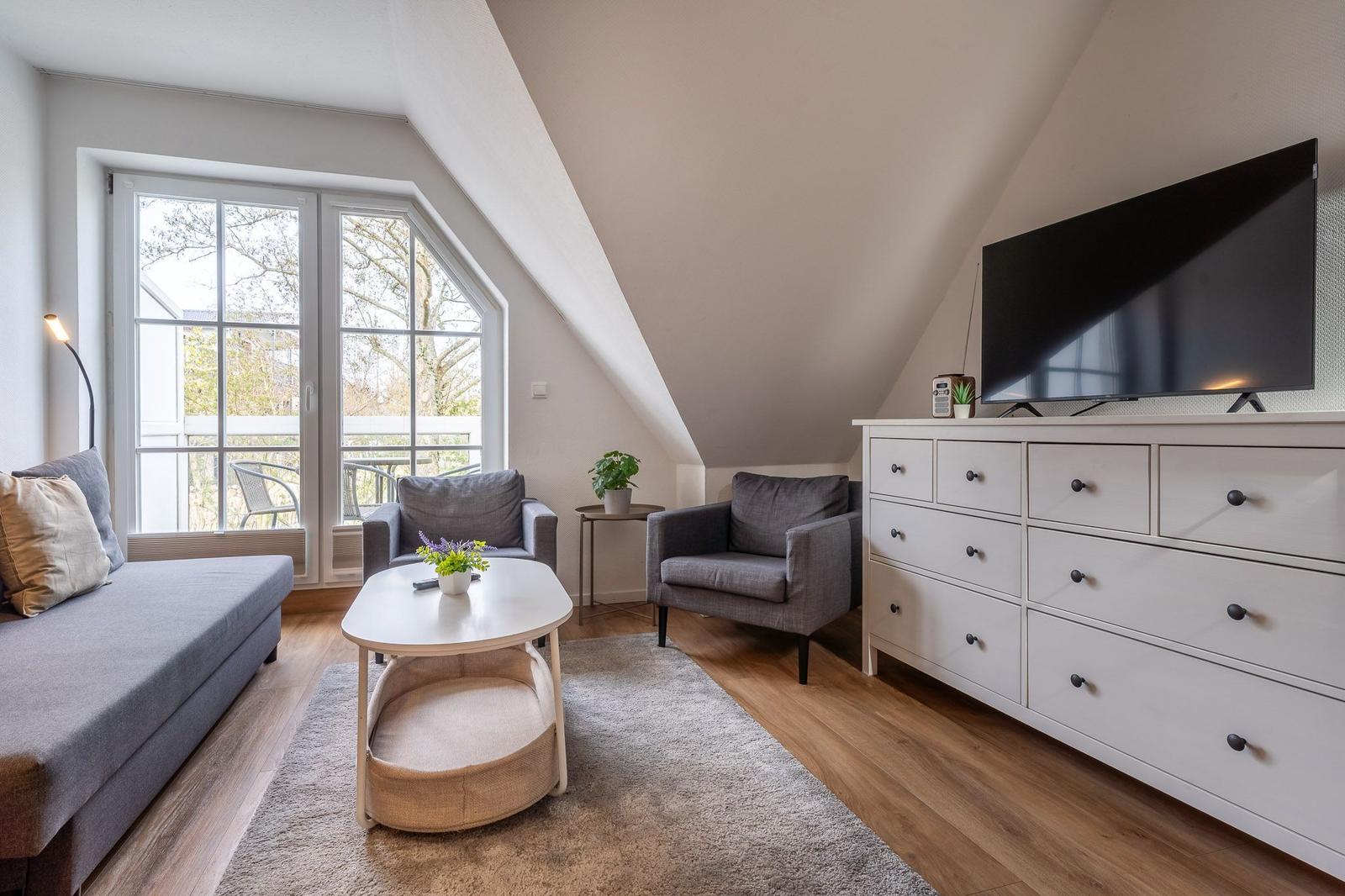 Wohnzimmer mit Schlafsofa, zwei Sesseln, Couchtisch und Fernseher auf Schrank