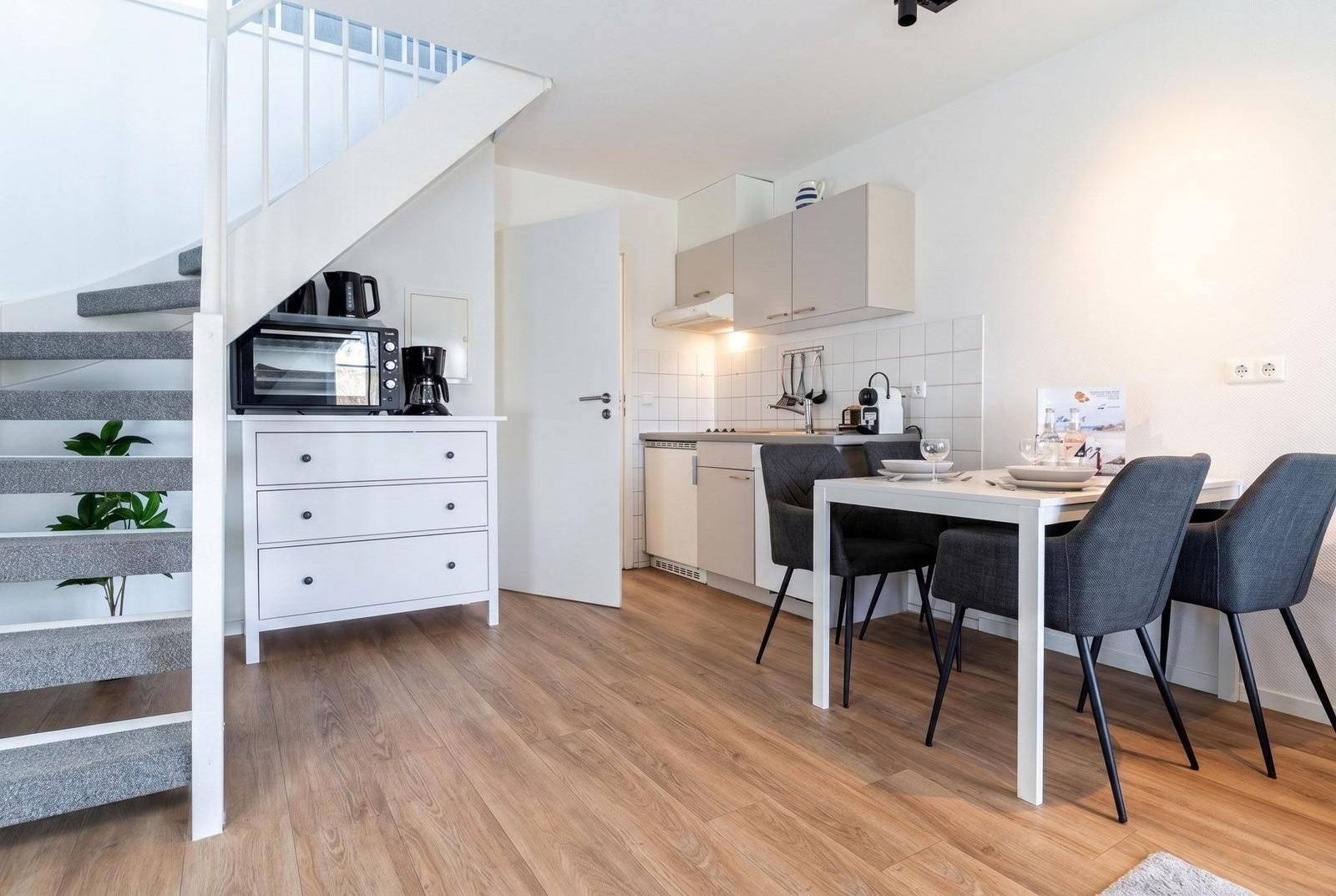 Küche mit Essbereich, Treppe und Holzboden. Weiße Möbel und graue Stühle.