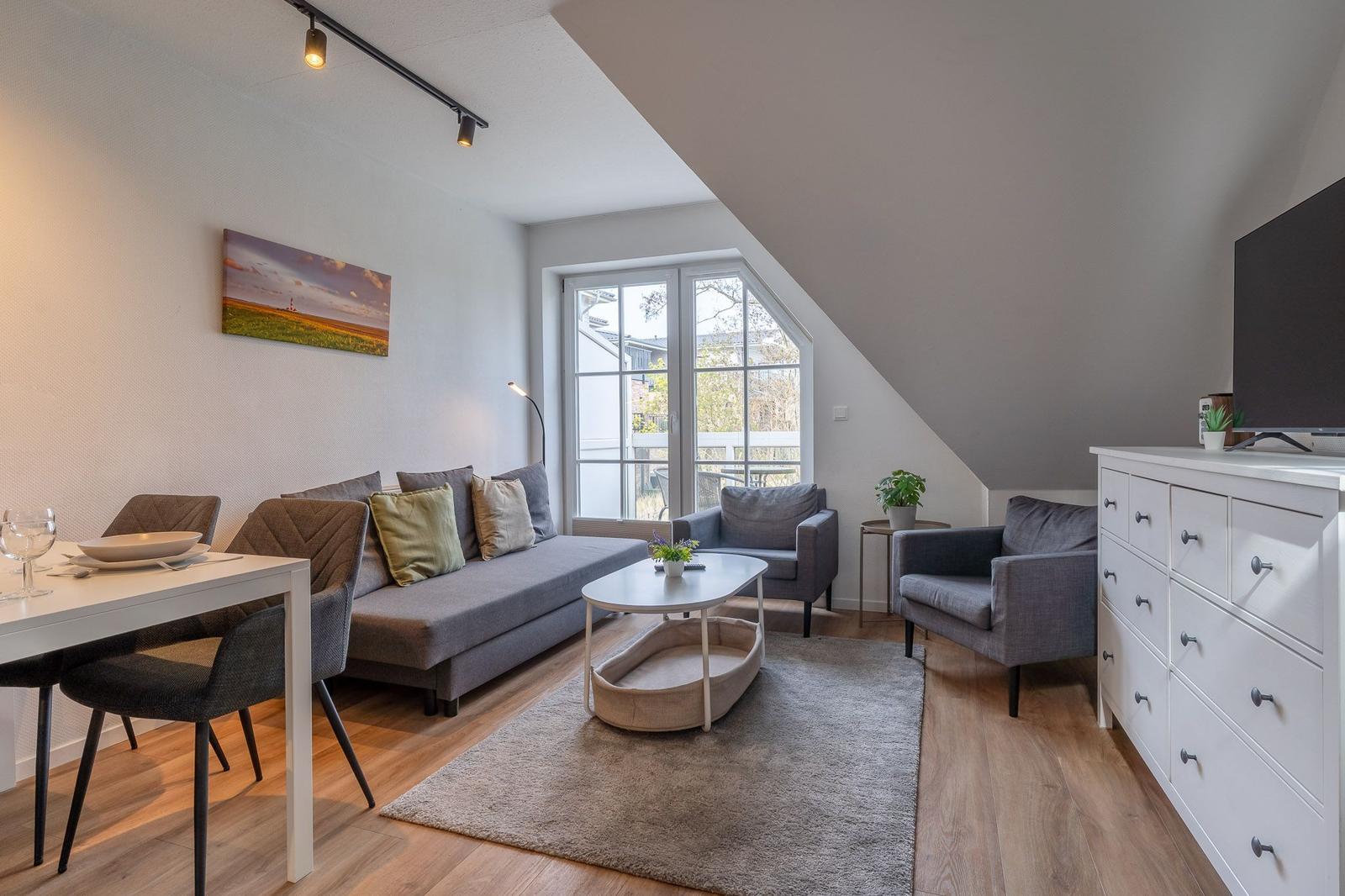 Wohnbereich mit Sofa, Sesseln, Esstisch und TV-Schrank unter Dachschräge.