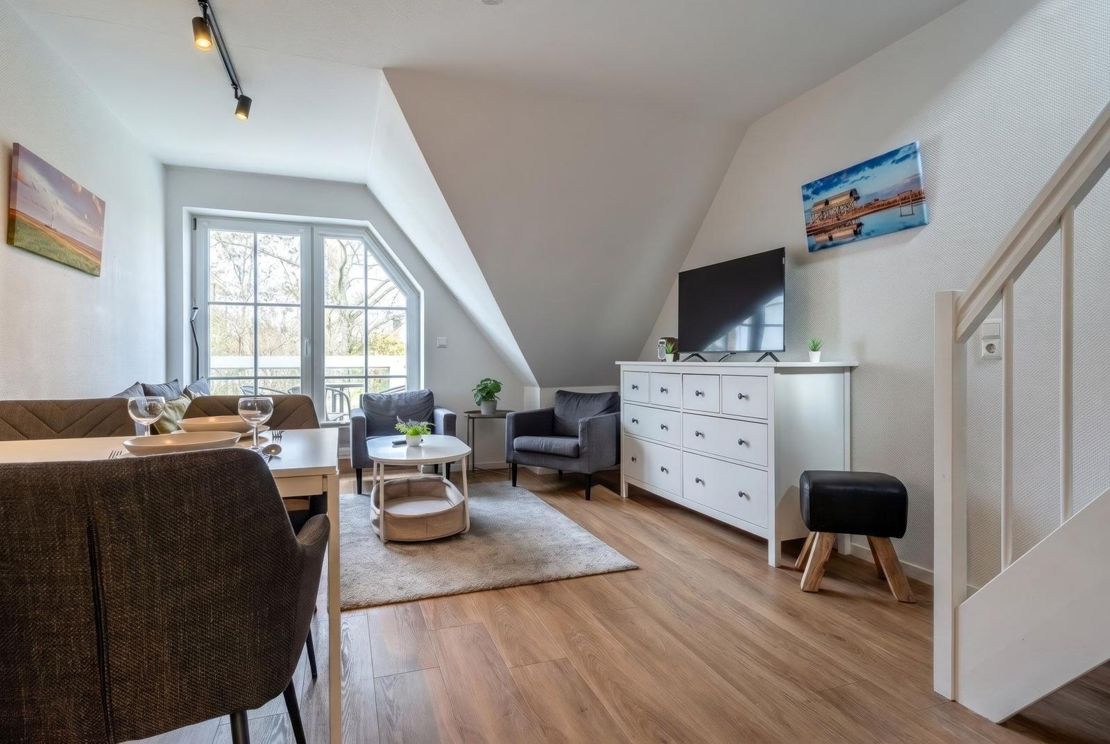 Wohn- und Essbereich mit Holzboden, TV-Schrank und Fenster zur Terrasse.