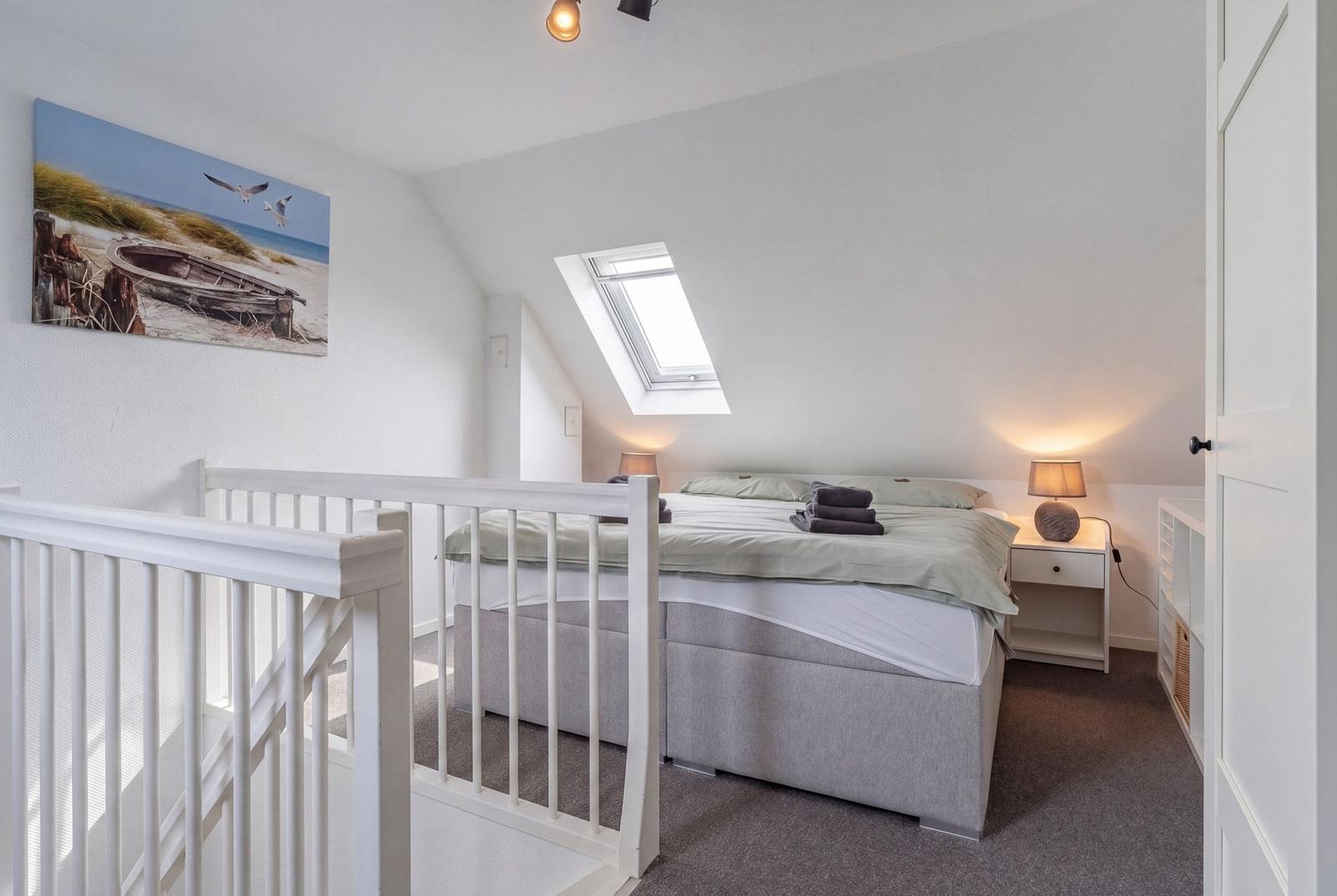 Schlafzimmer mit Dachschrägen, Dachfenster und Bett mit Nachttischen.