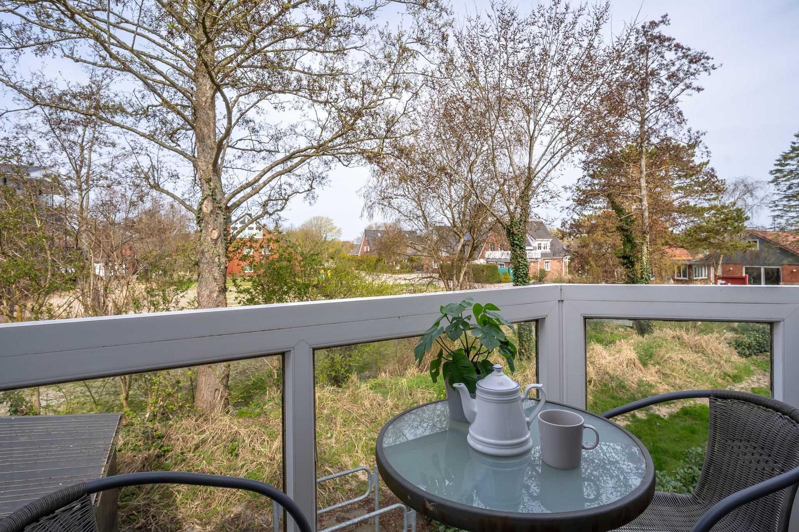 Terrasse mit Tisch, Stühlen und Blick auf Bäume und Häuser.
