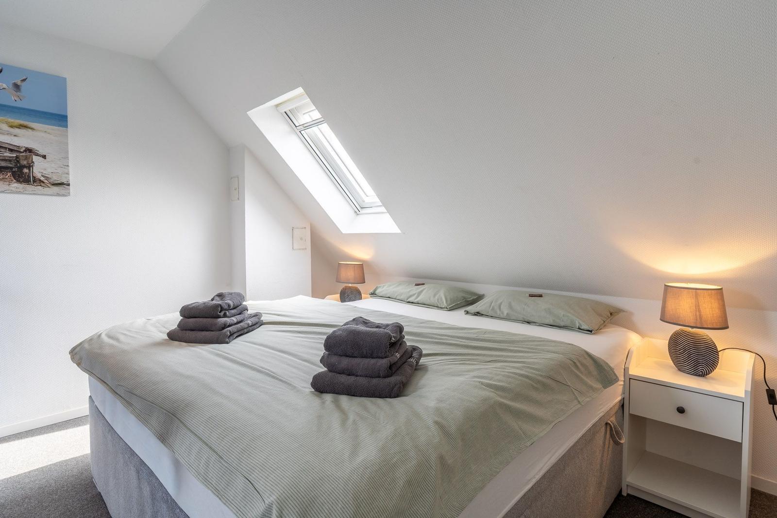 Schlafzimmer mit Dachschrägen, Dachfenster und Bett mit Handtüchern.