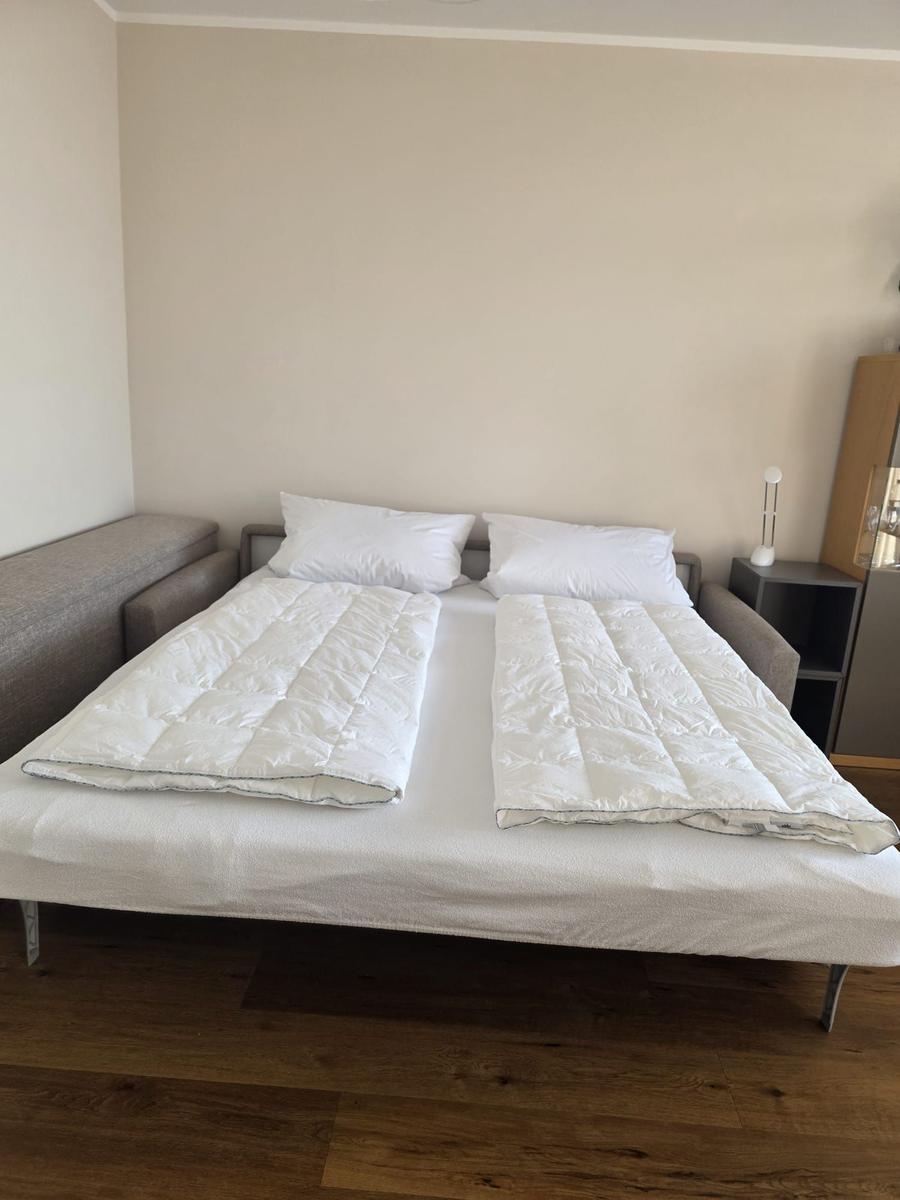 Schlafzimmer mit Doppelbett, weißen Kissen und Decken, Holzboden und Nachttisch.