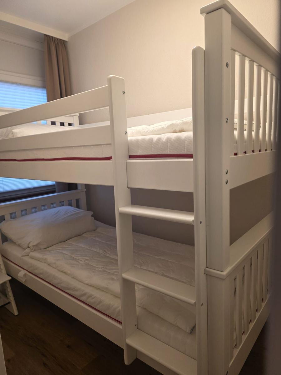Ein weißes Doppelstockbett mit Matratzen und Kissen.