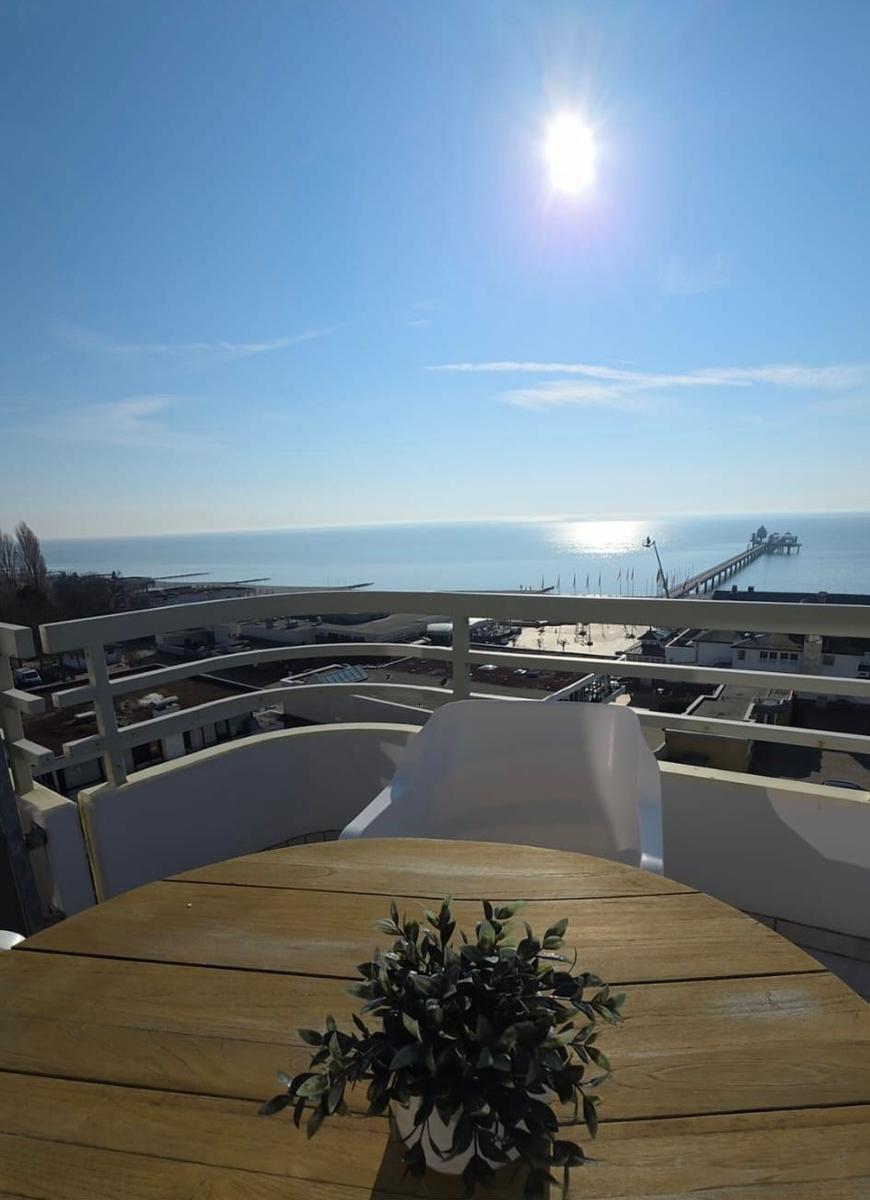 Terrasse mit Tisch und Stuhl. Blick auf Meer und Pier bei sonnigem Wetter.