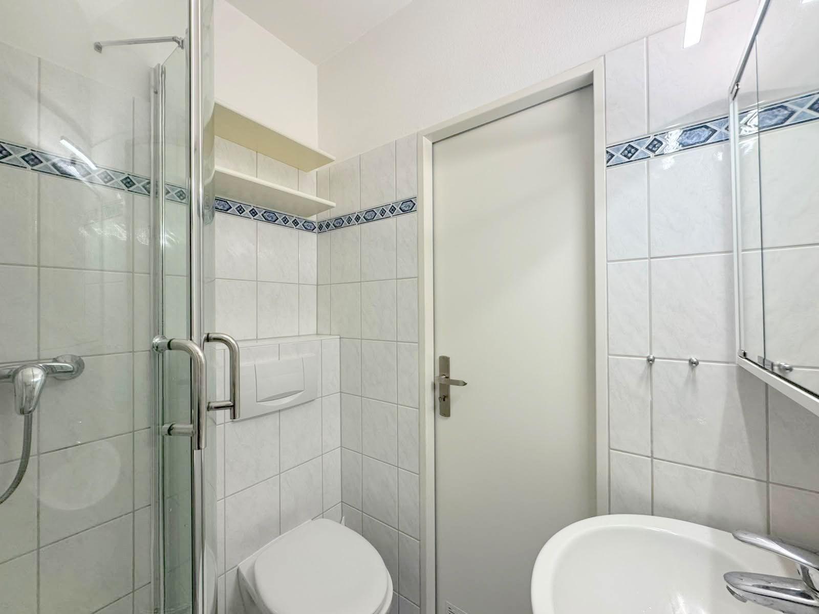 Badezimmer mit Dusche, Toilette und Waschbecken. Fliesen mit blauem Muster.