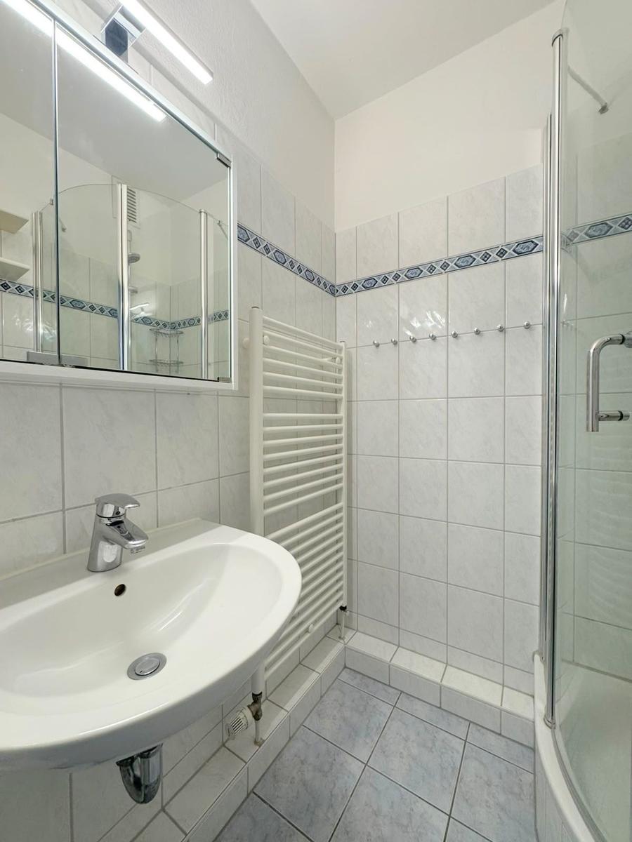 Badezimmer mit Dusche, Waschbecken und Heizkörper