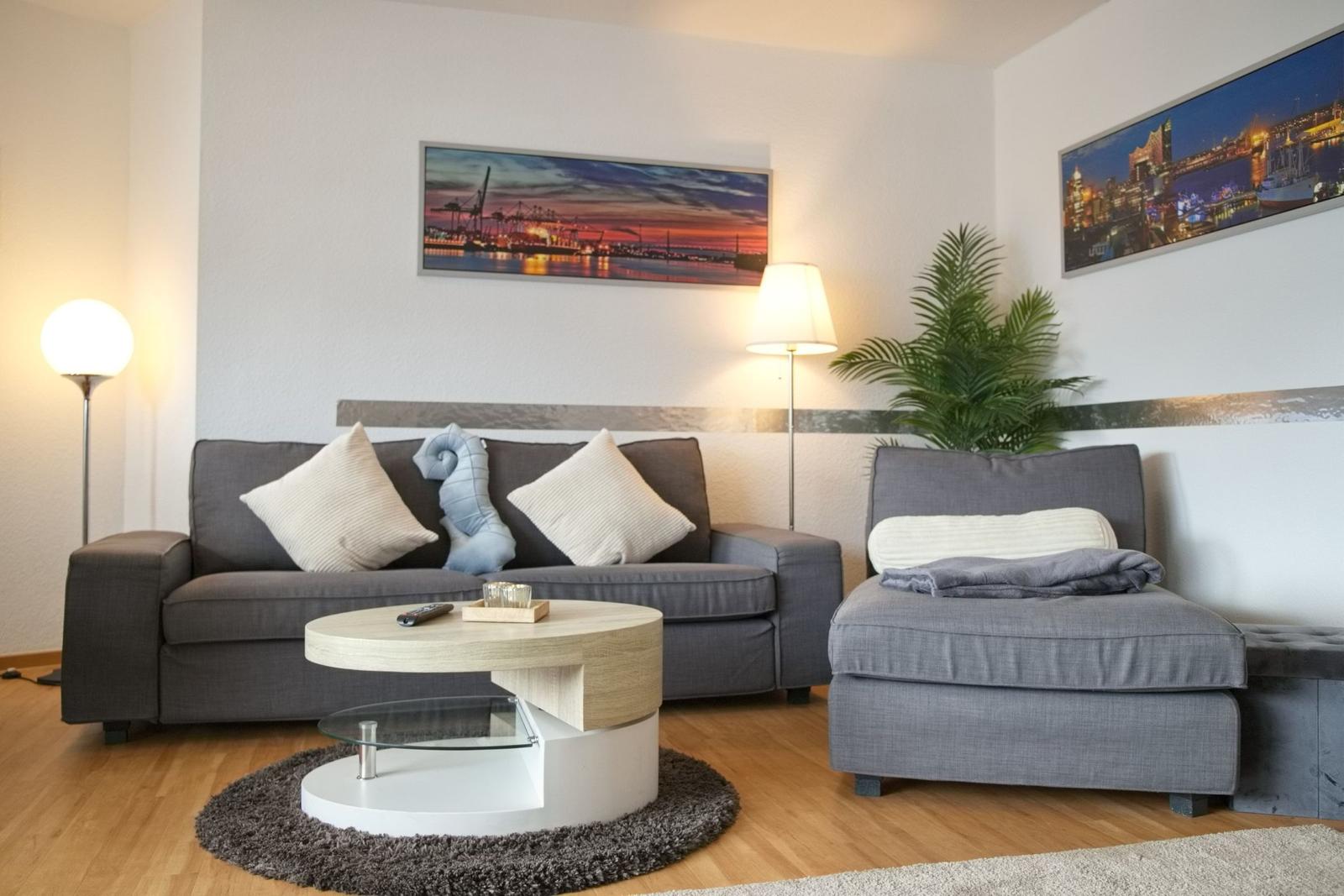 Wohnzimmer mit grauem Sofa, runden Couchtisch und Wandbildern