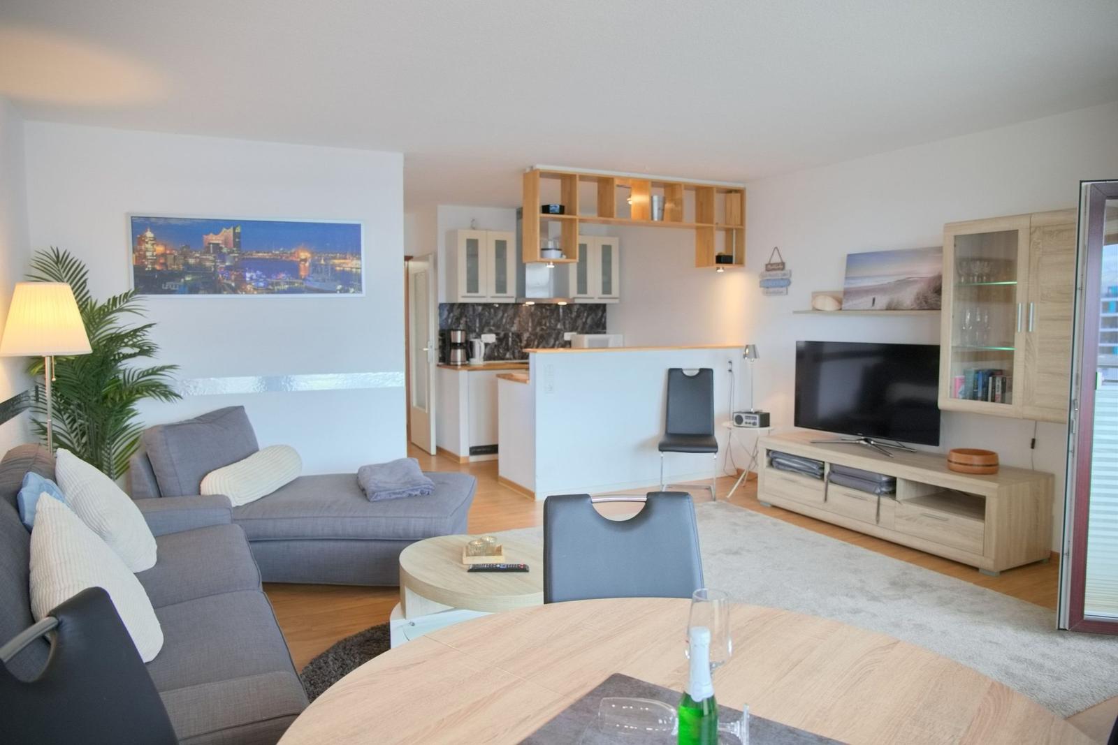 Wohnbereich mit Sofa, Essplatz und Küchenbereich. Fernseher und Garderobe sind vorhanden.