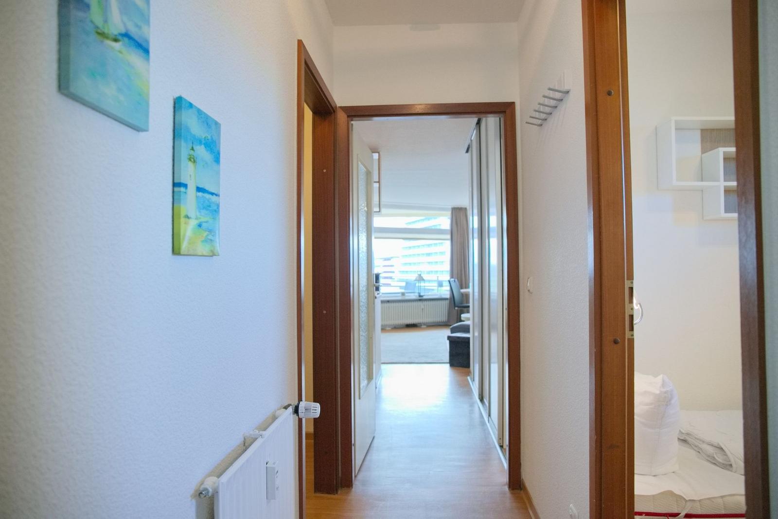 Flur mit Türen zu Schlafzimmer und Wohnbereich, Wandbilder und Heizkörper sichtbar.