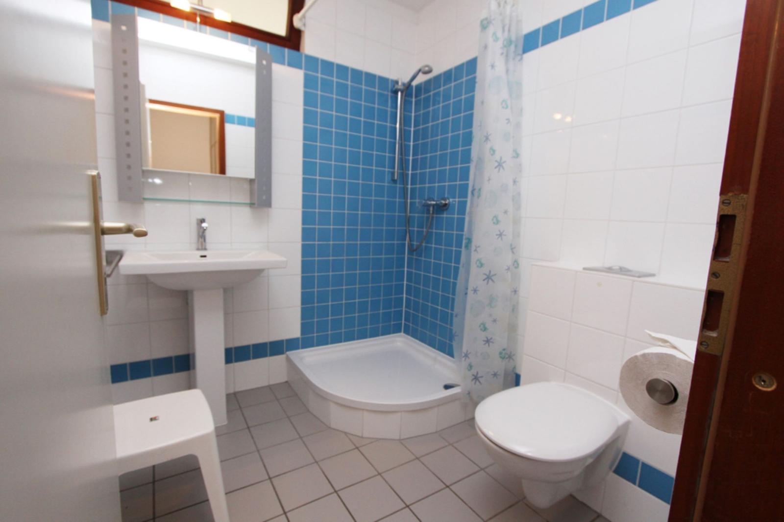 Badezimmer mit Dusche, Waschbecken und Toilette. Blaue Fliesen an einer Wand.
