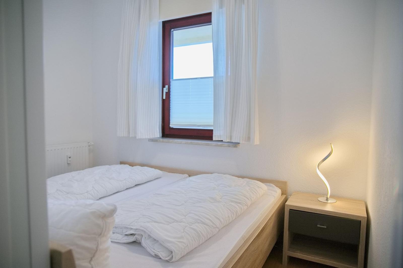 Ein Schlafzimmer mit Bett, Nachttisch und Fenster mit Vorhängen.