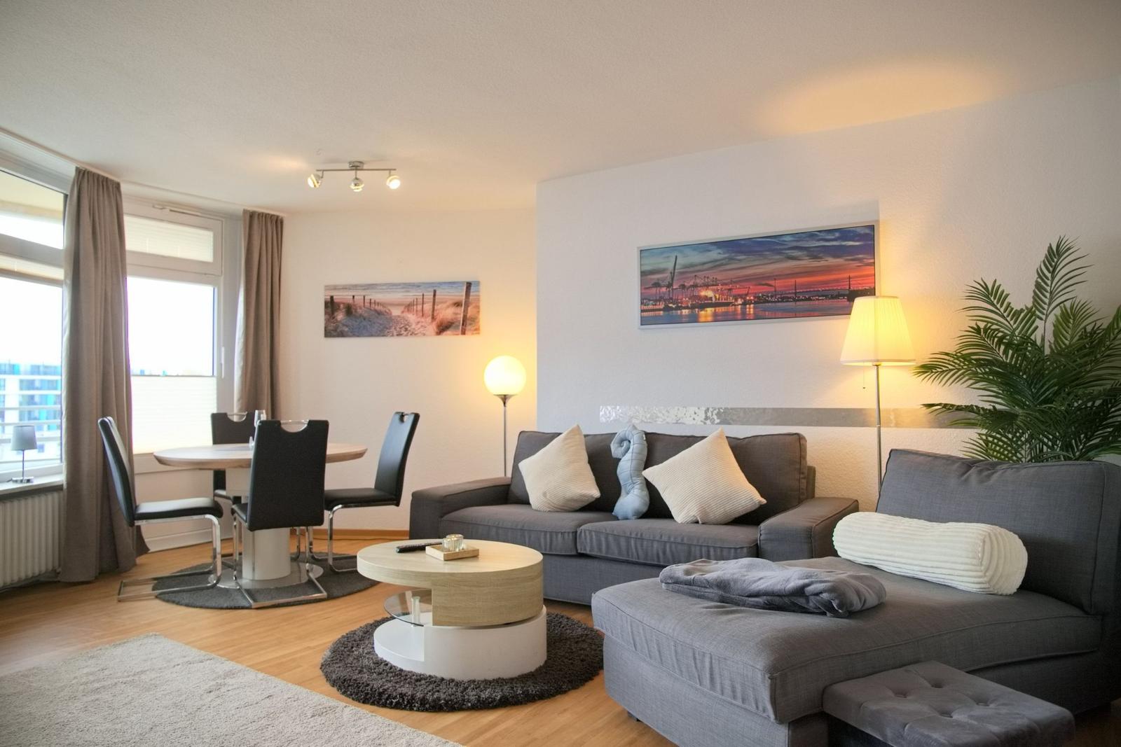 Wohn- und Essbereich mit Sofa, Tisch und Fenster. Wandbilder und Pflanze.