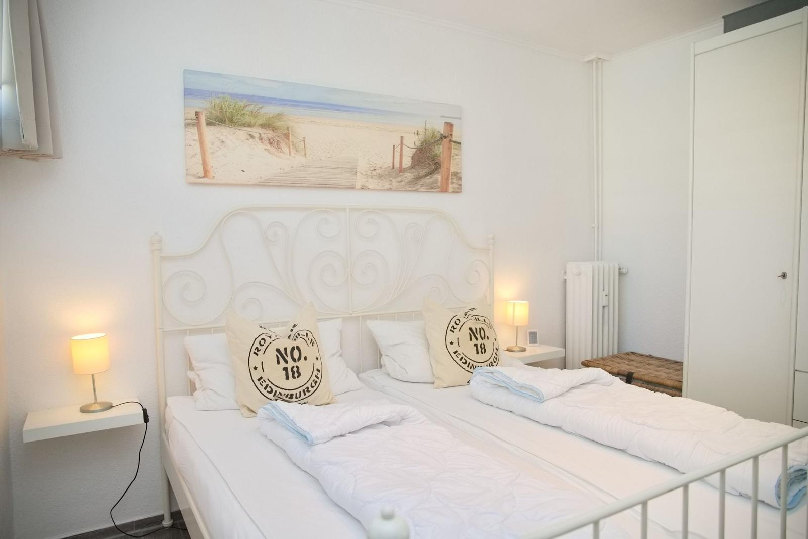 Schlafzimmer mit Doppelbett, Wandbild und Nachttischen mit Lampen.